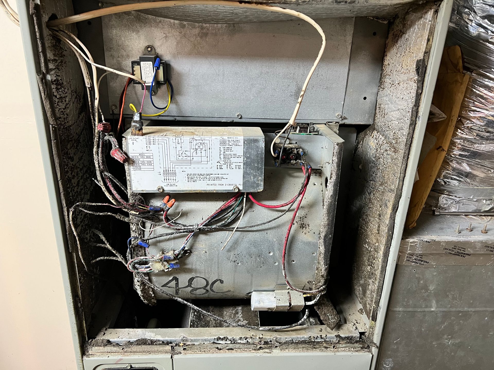 The inside of a dirty air conditioner with a lot of wires coming out of it.