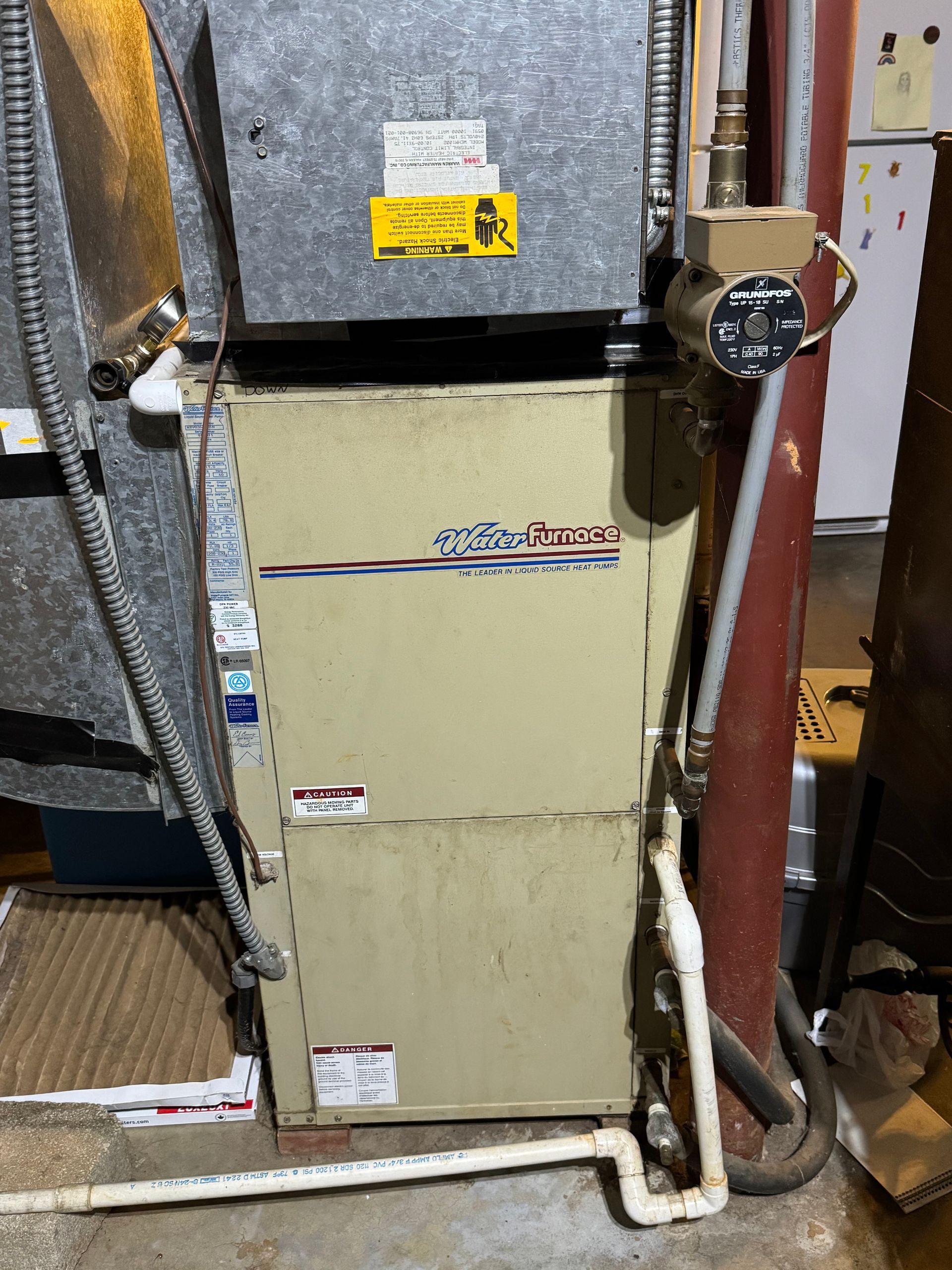 A furnace is sitting in a basement next to a refrigerator.