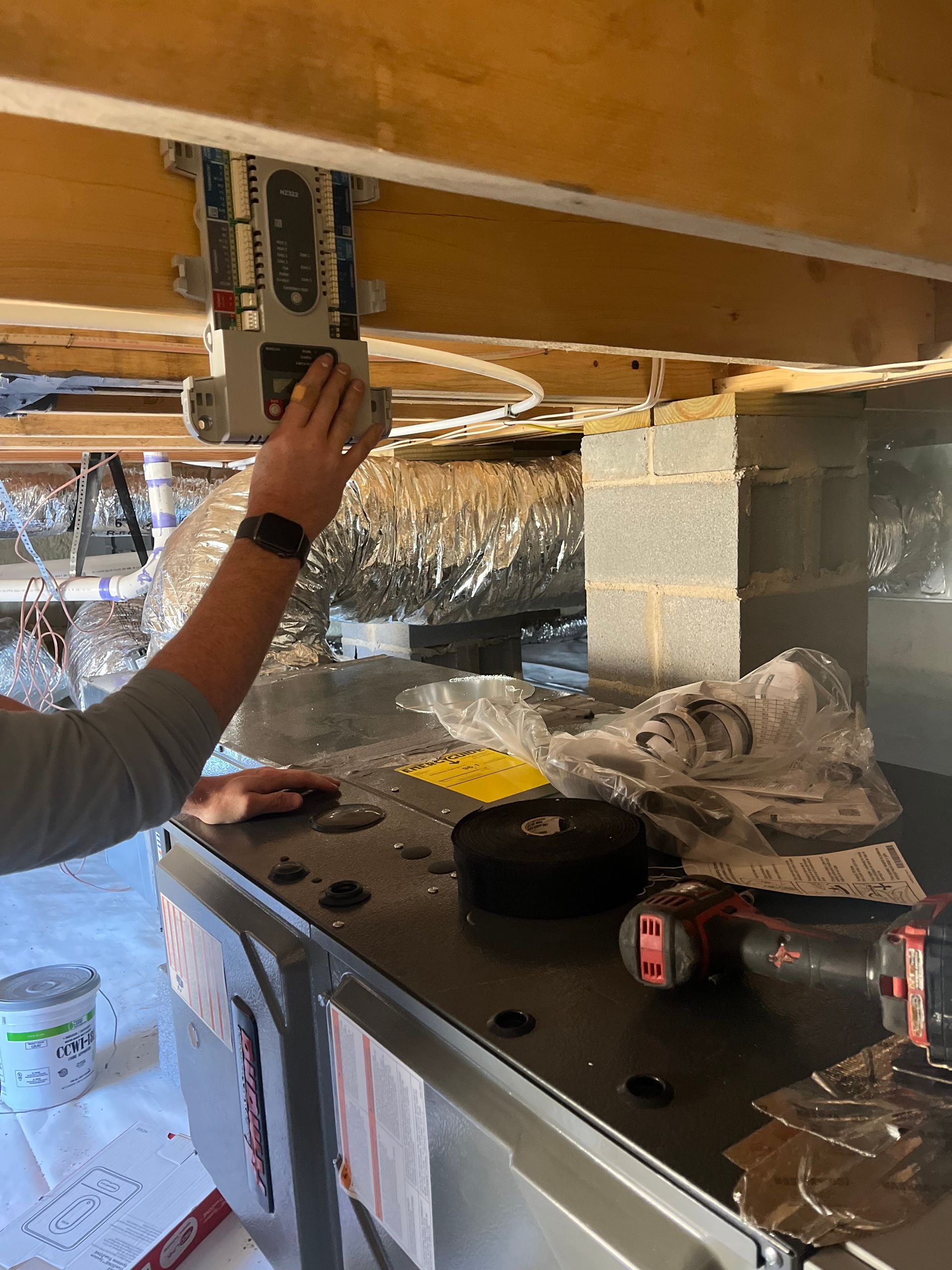 A man is working on an air conditioner in a basement.