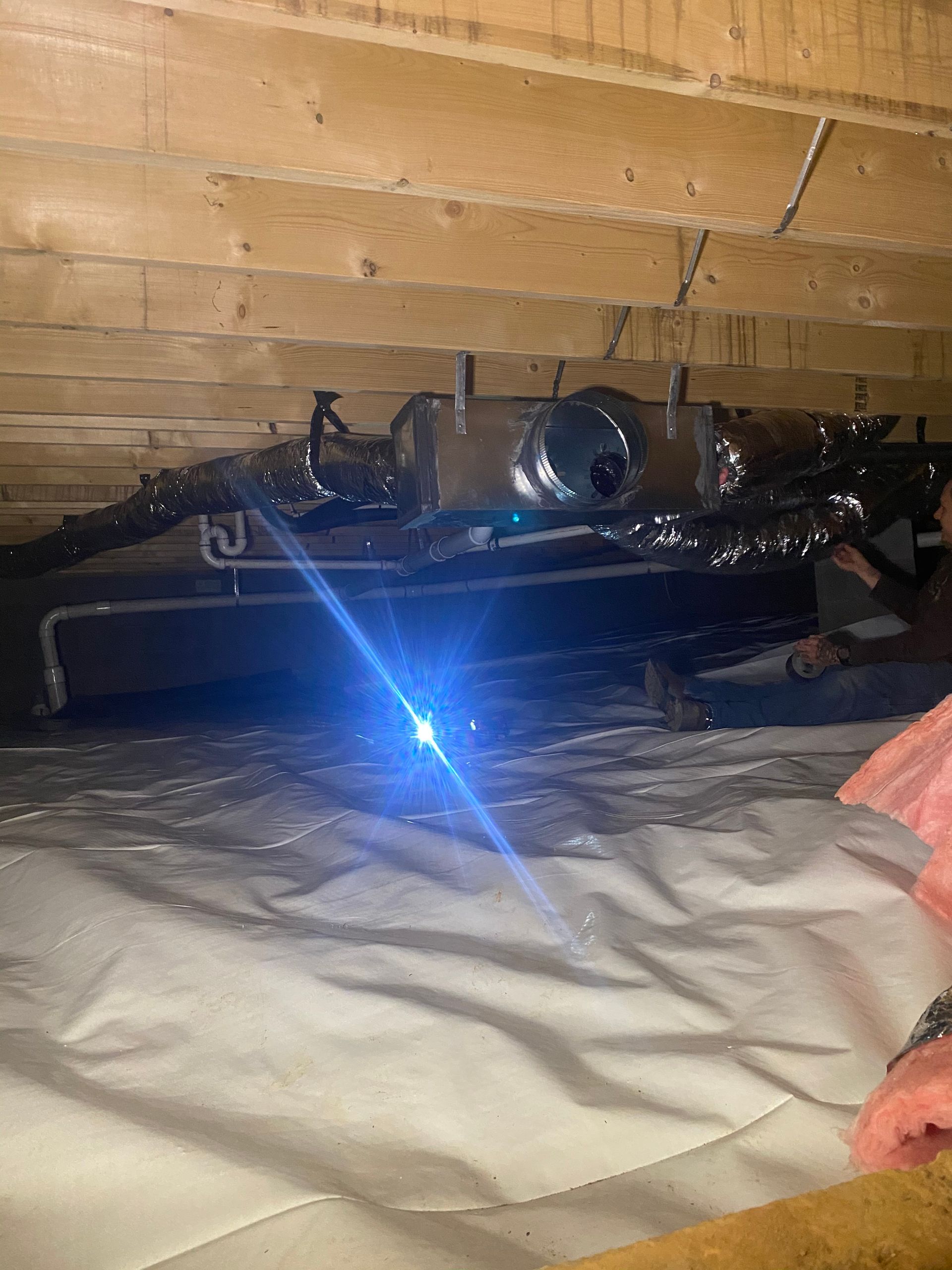 A person is laying in a basement with a light shining through the ceiling.