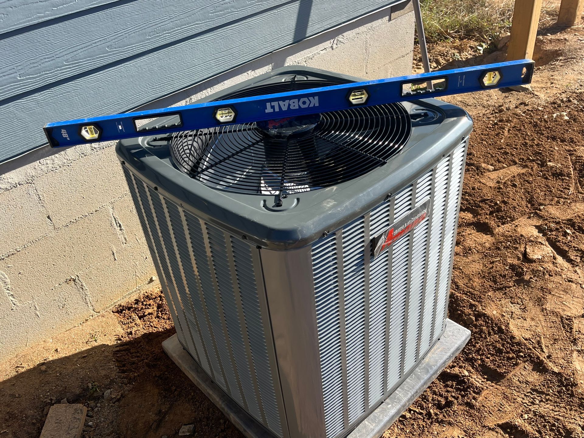 A blue level is sitting on top of an air conditioner.