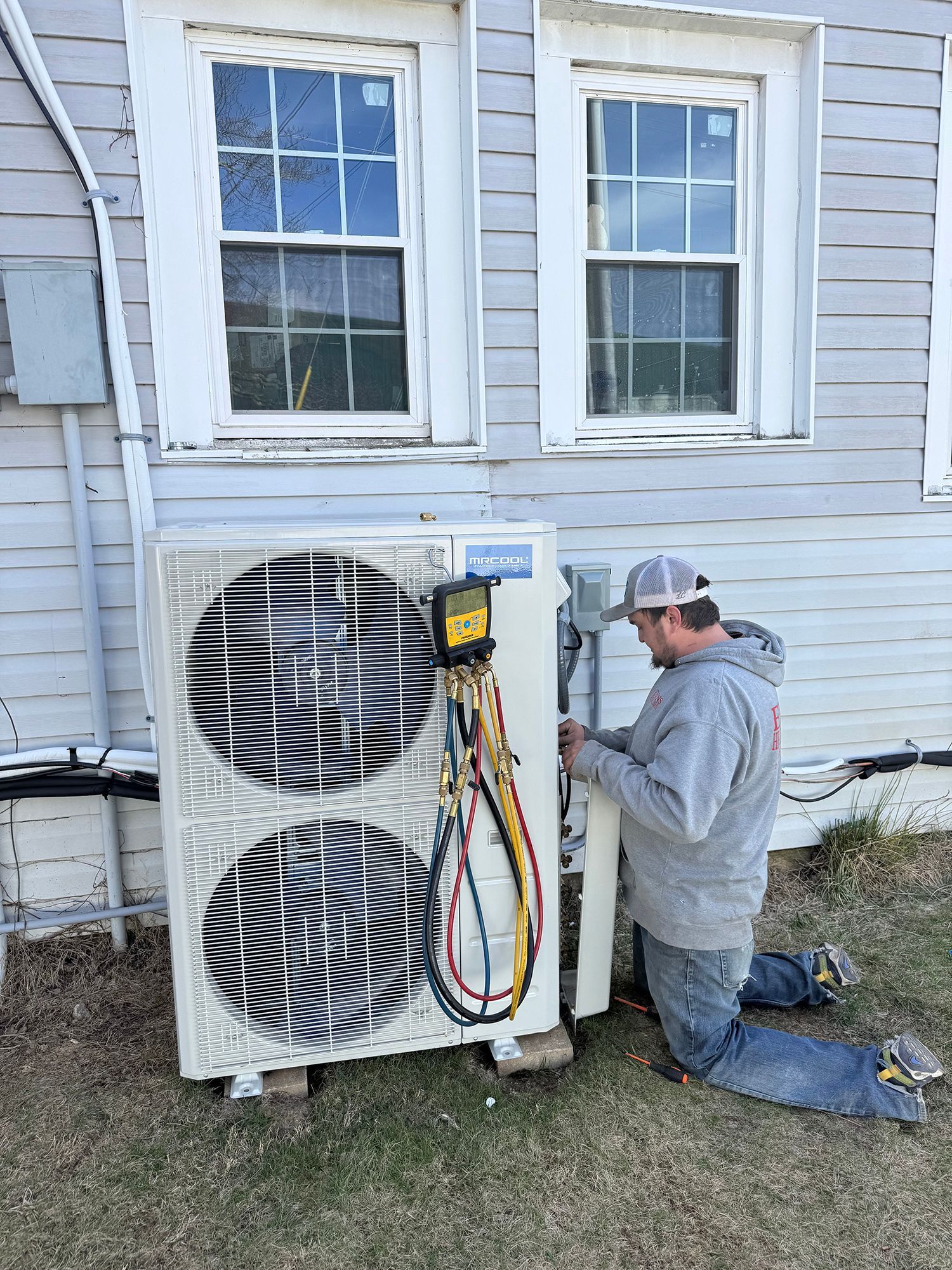 A man is working on an air conditioner outside of a house.