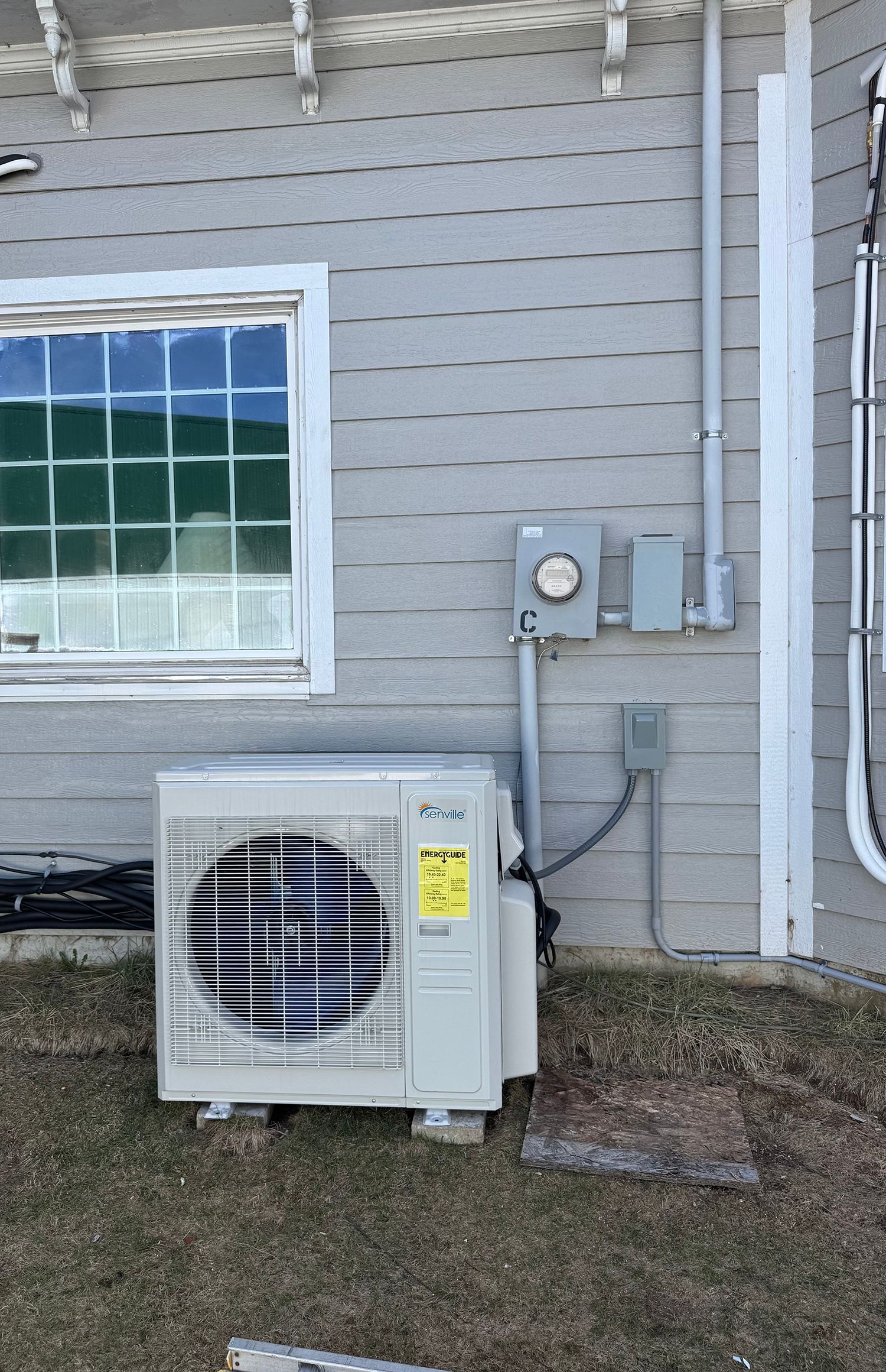 An air conditioner is sitting on the side of a house next to a window.