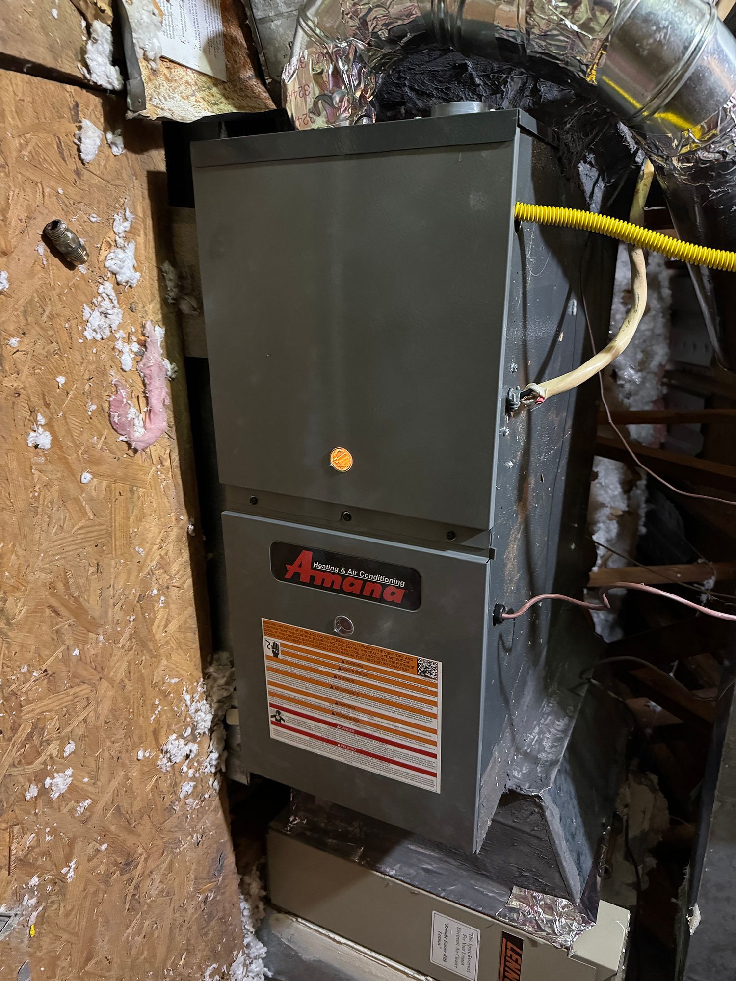 A furnace is sitting in a basement next to a wall.