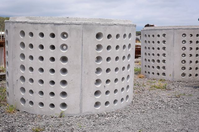 Concrete cylindrical blocks with rows of round holes on a gravel surface outdoors