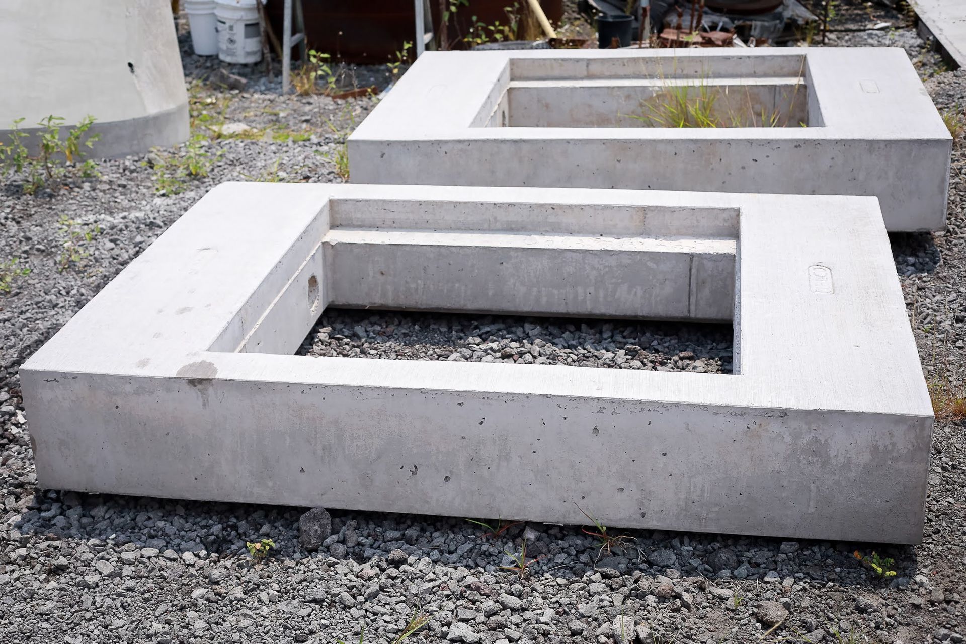 Rectangular concrete bench or planter blocks on gravel, with open centers and one on the ground in front