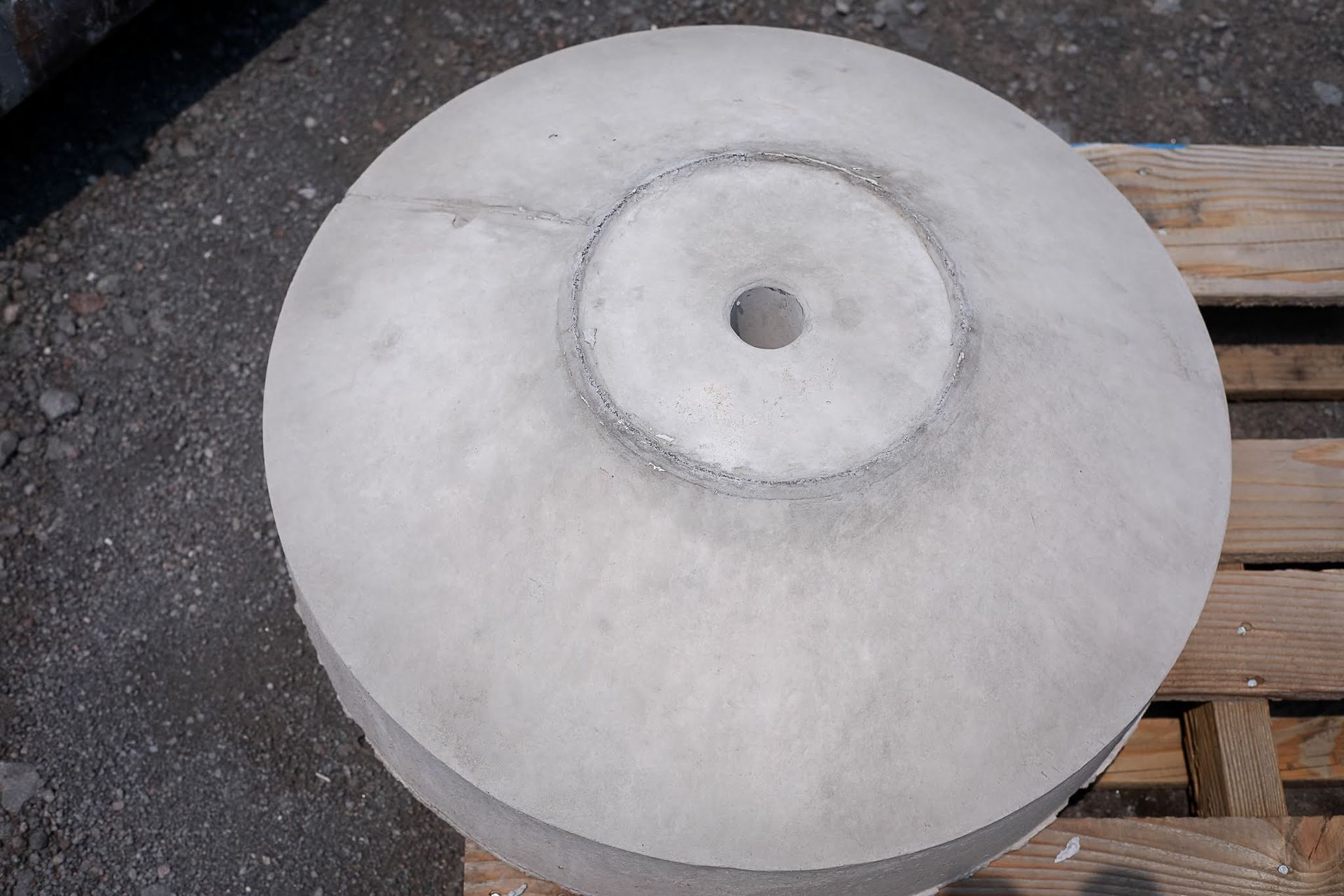 Gray circular concrete or stone disk with a central hole, resting on a wooden pallet outdoors.