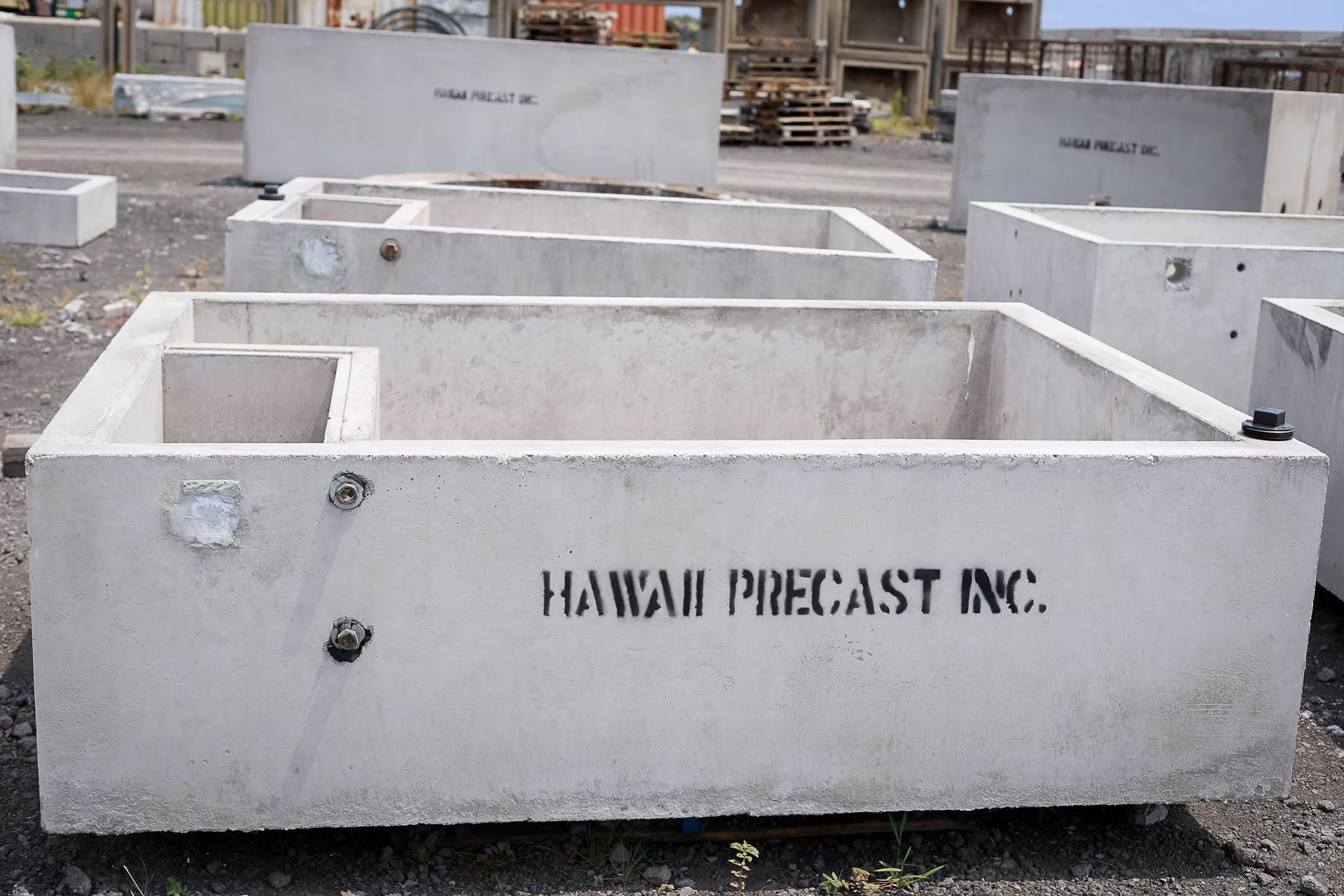 Concrete precast boxes in an outdoor yard, with “Hawaii Precast Inc.” printed on the front.