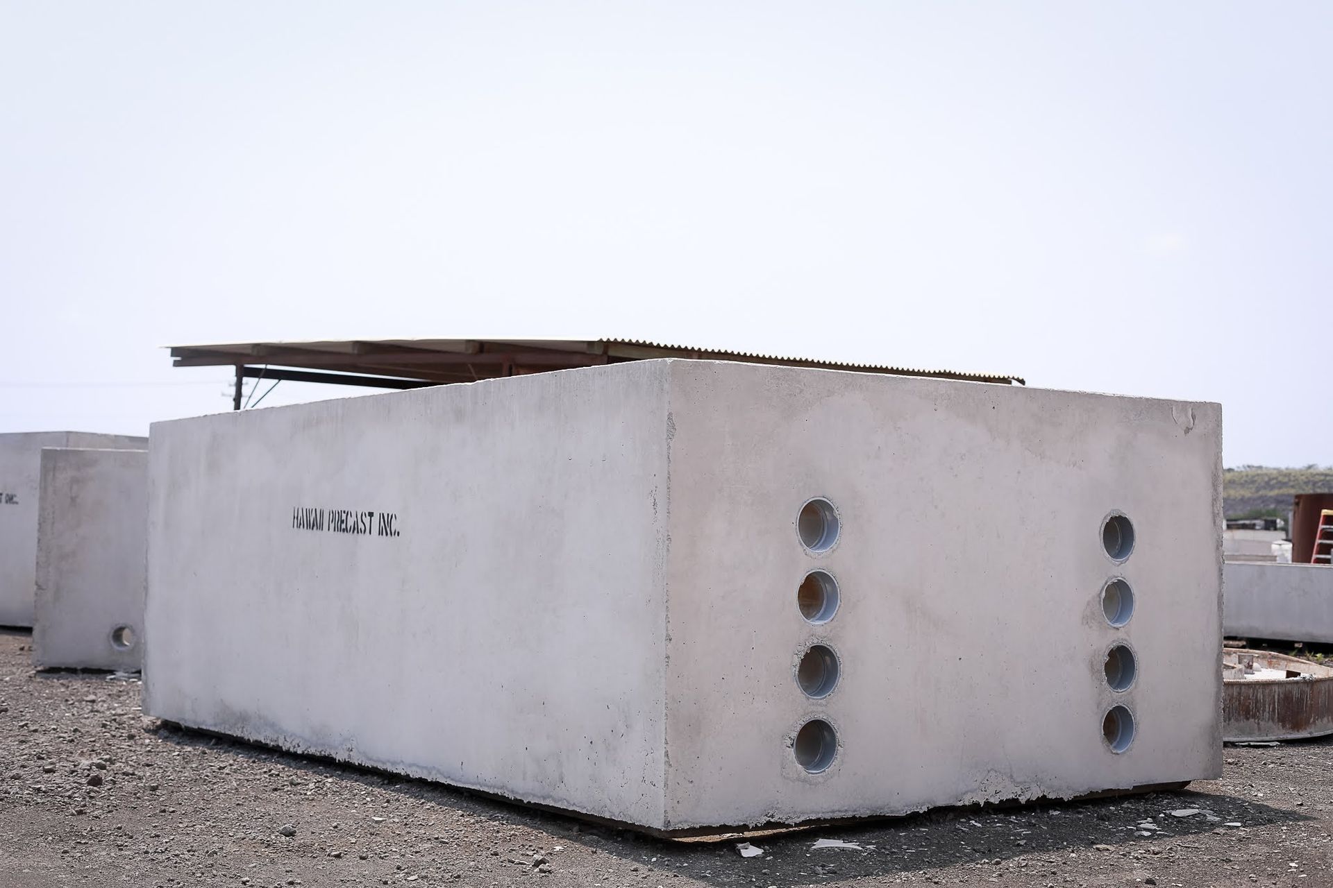 Concrete utility building with round vents, in a gravel lot under a cloudy sky