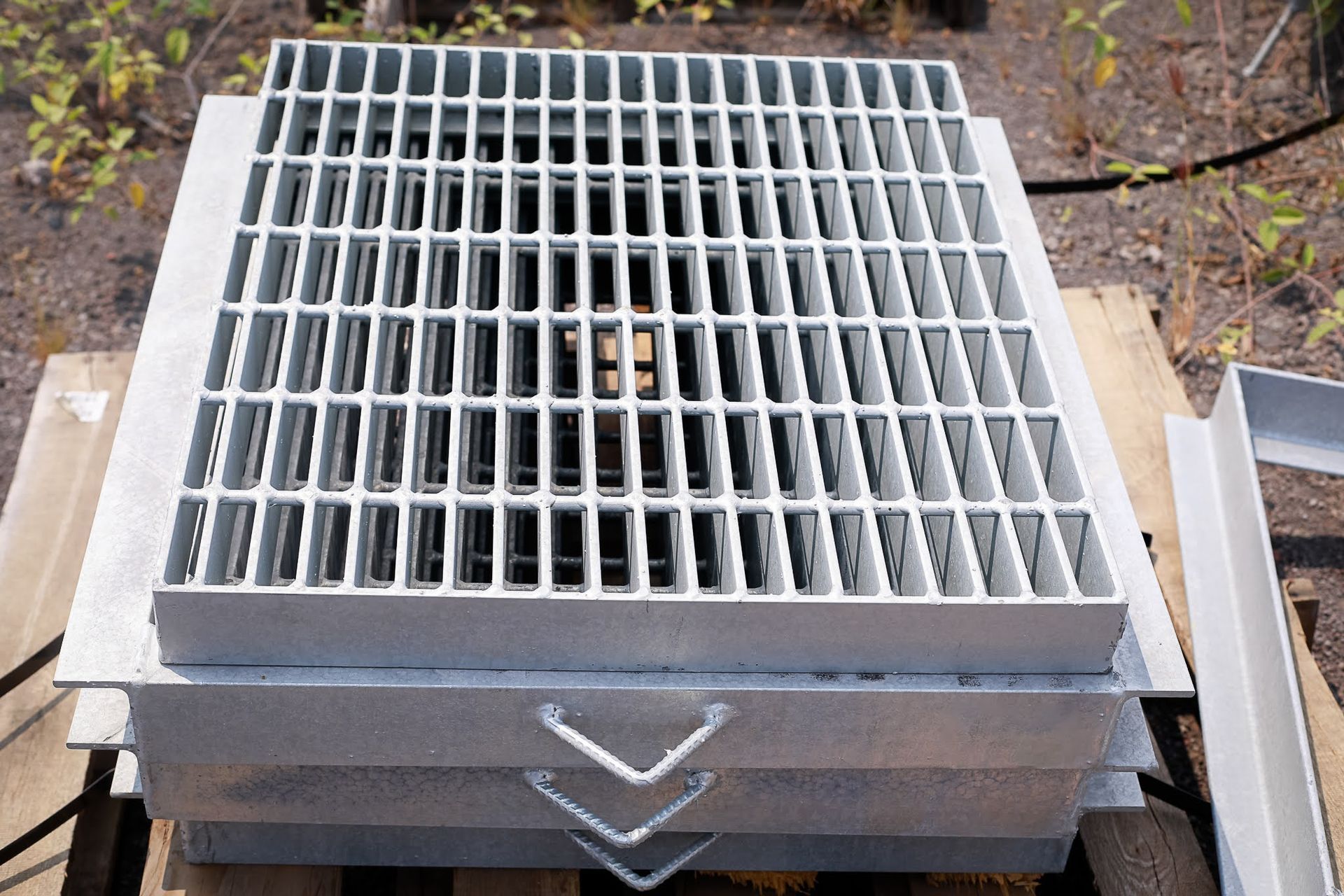 Metal grate-covered utility hatch with three chevron markings, set outdoors on a concrete surface.