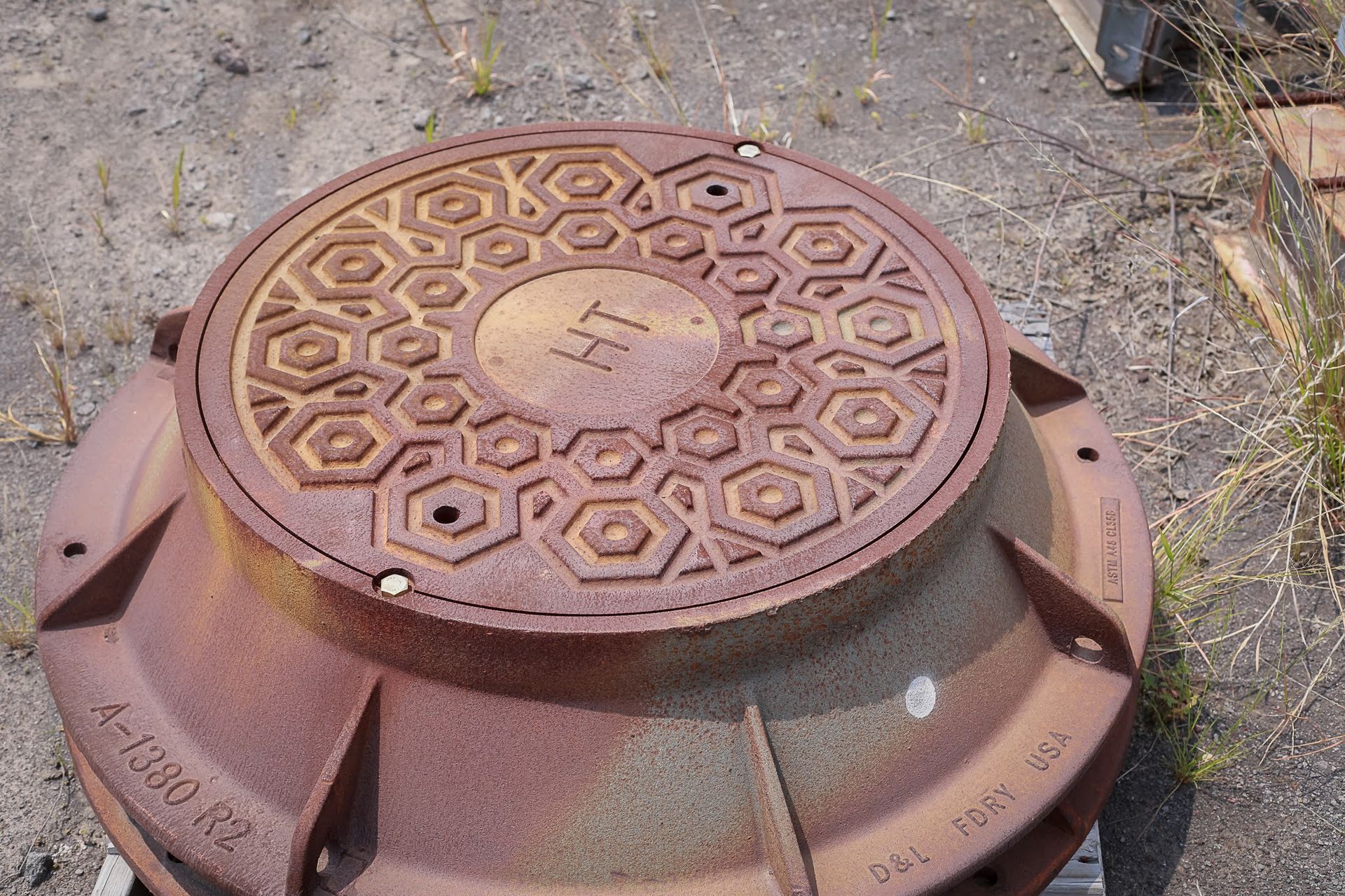 Rusty metal manhole cover on pavement with patterned circular lid and bolts