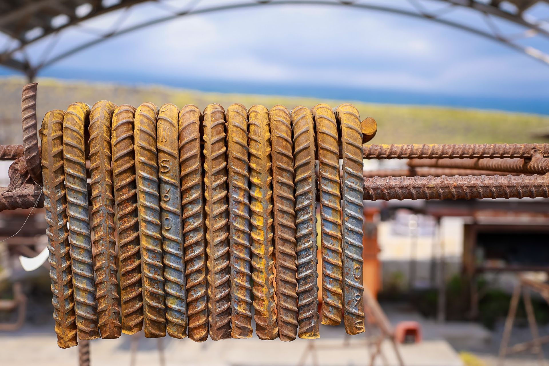 Rows of gold and brown dried fish hanging outdoors on metal racks under a blue sky