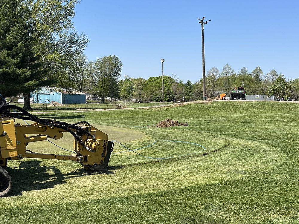 A yellow trenching machine cutting a curved line in a grassy field on a sunny day.