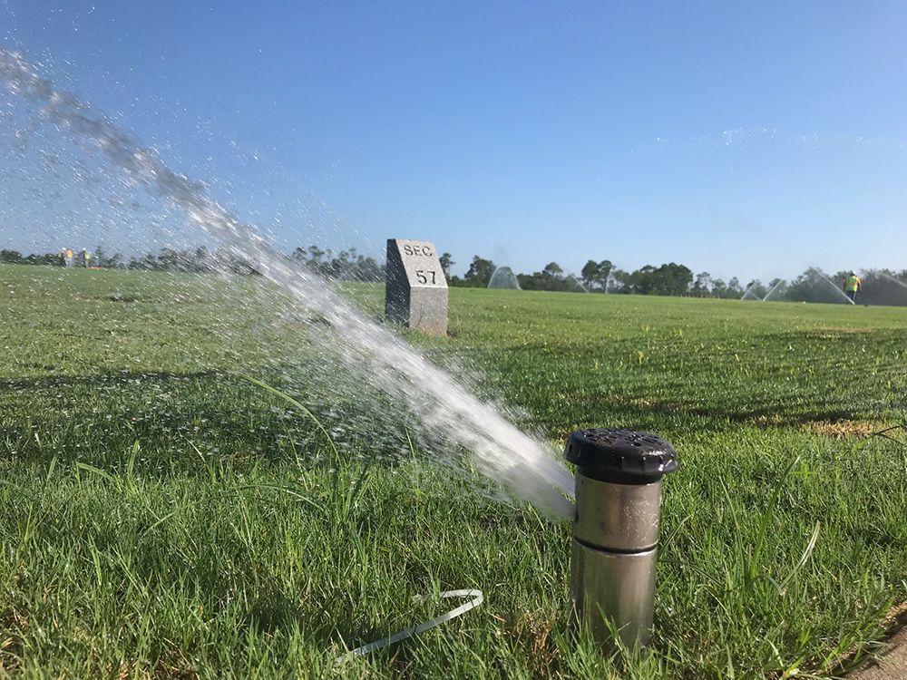 Sprinkler spraying water onto a green field under a clear blue sky.