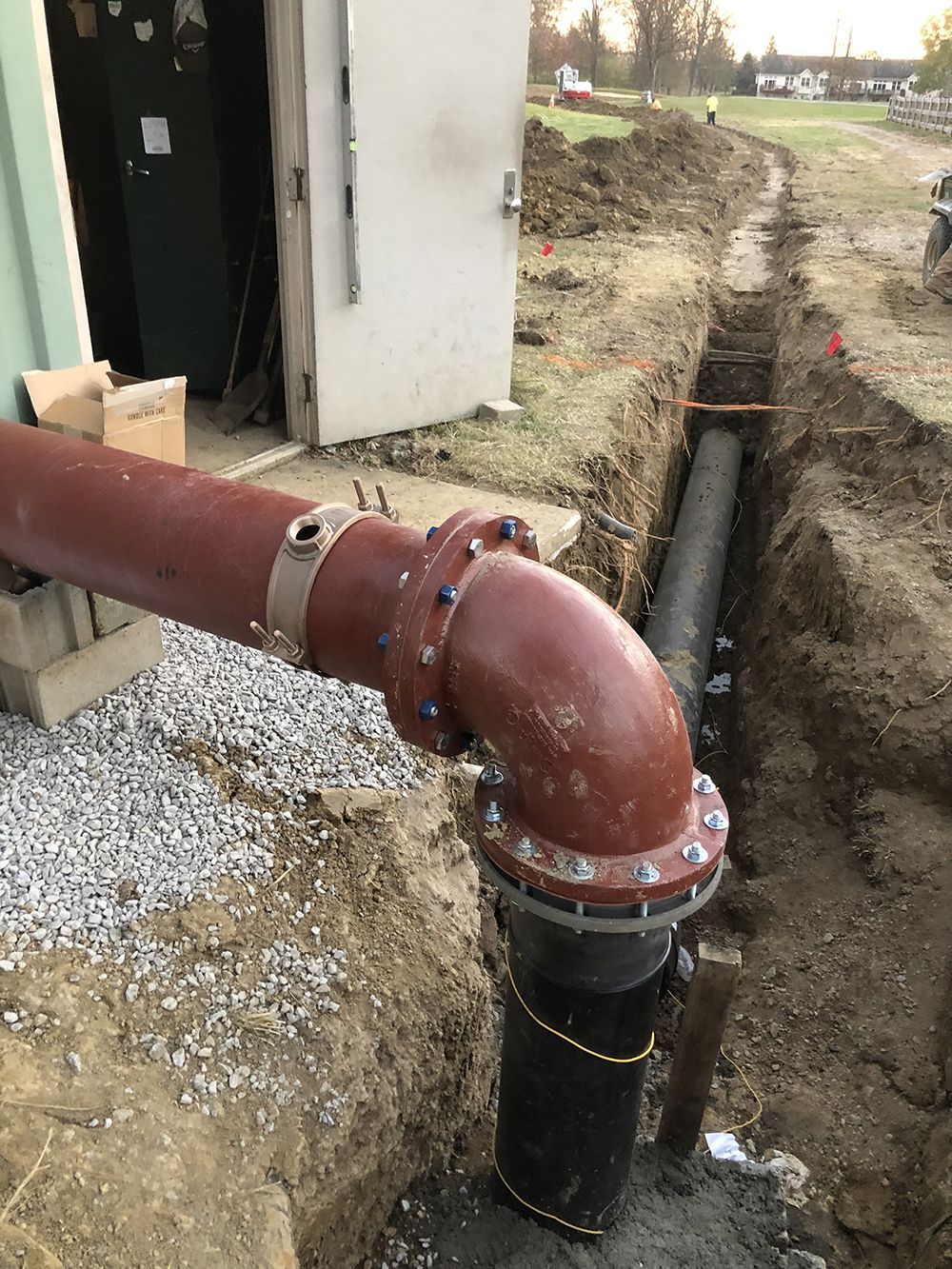 Red and black pipes in a trench next to a building, indicating construction.