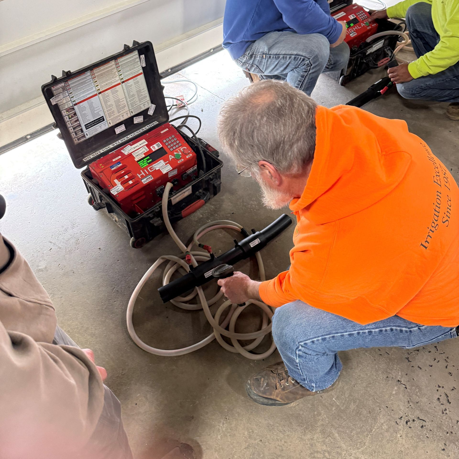 Man in orange hoodie operates equipment connected to a control panel, likely for testing, in an indoor setting.