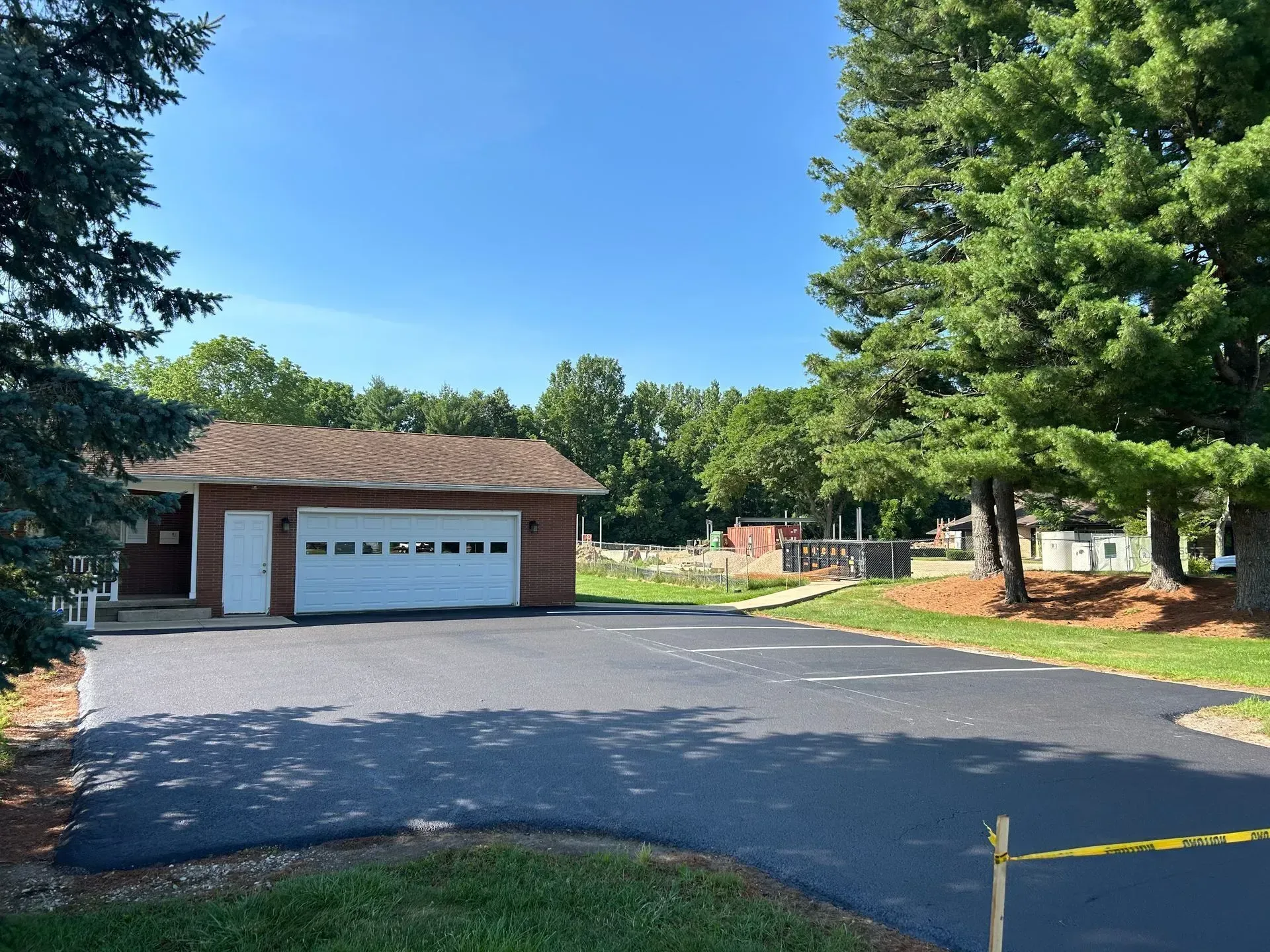 Brick house with white garage door on a tree-lined driveway under a clear blue sky
