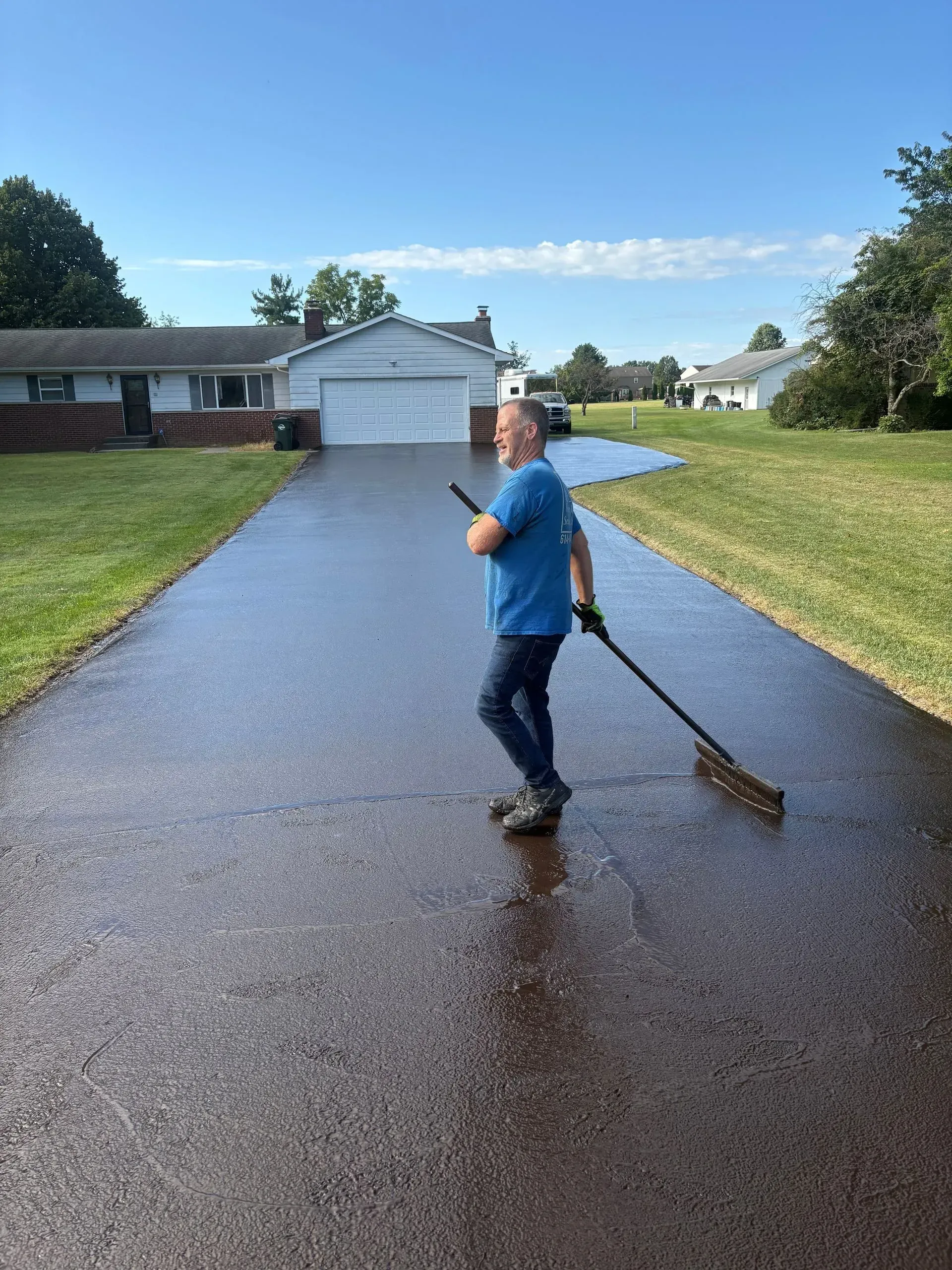 Person sweeping a wet driveway in front of a house and garage on a sunny day