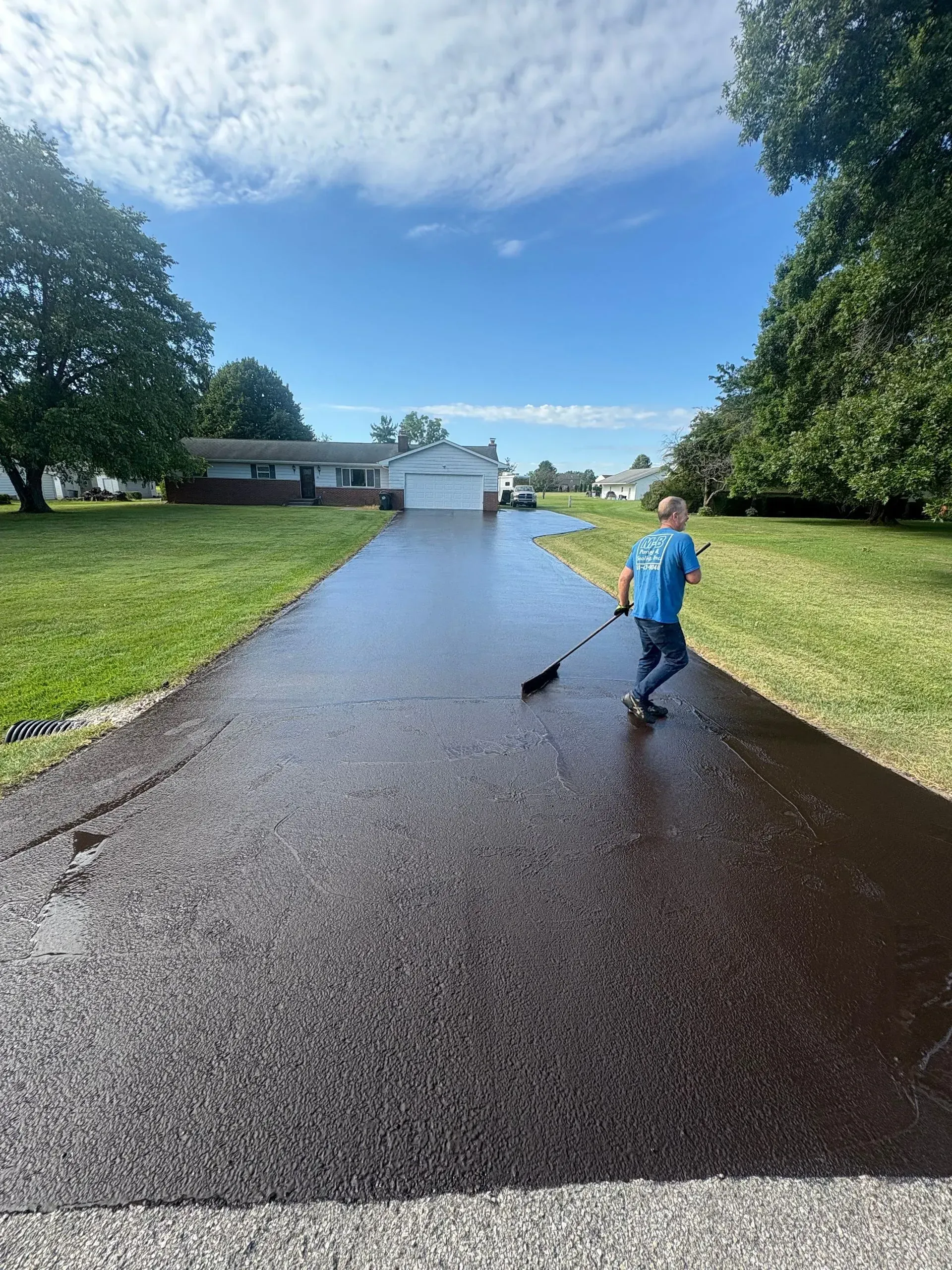 Child in blue riding a scooter down a freshly paved driveway toward a house on a sunny day