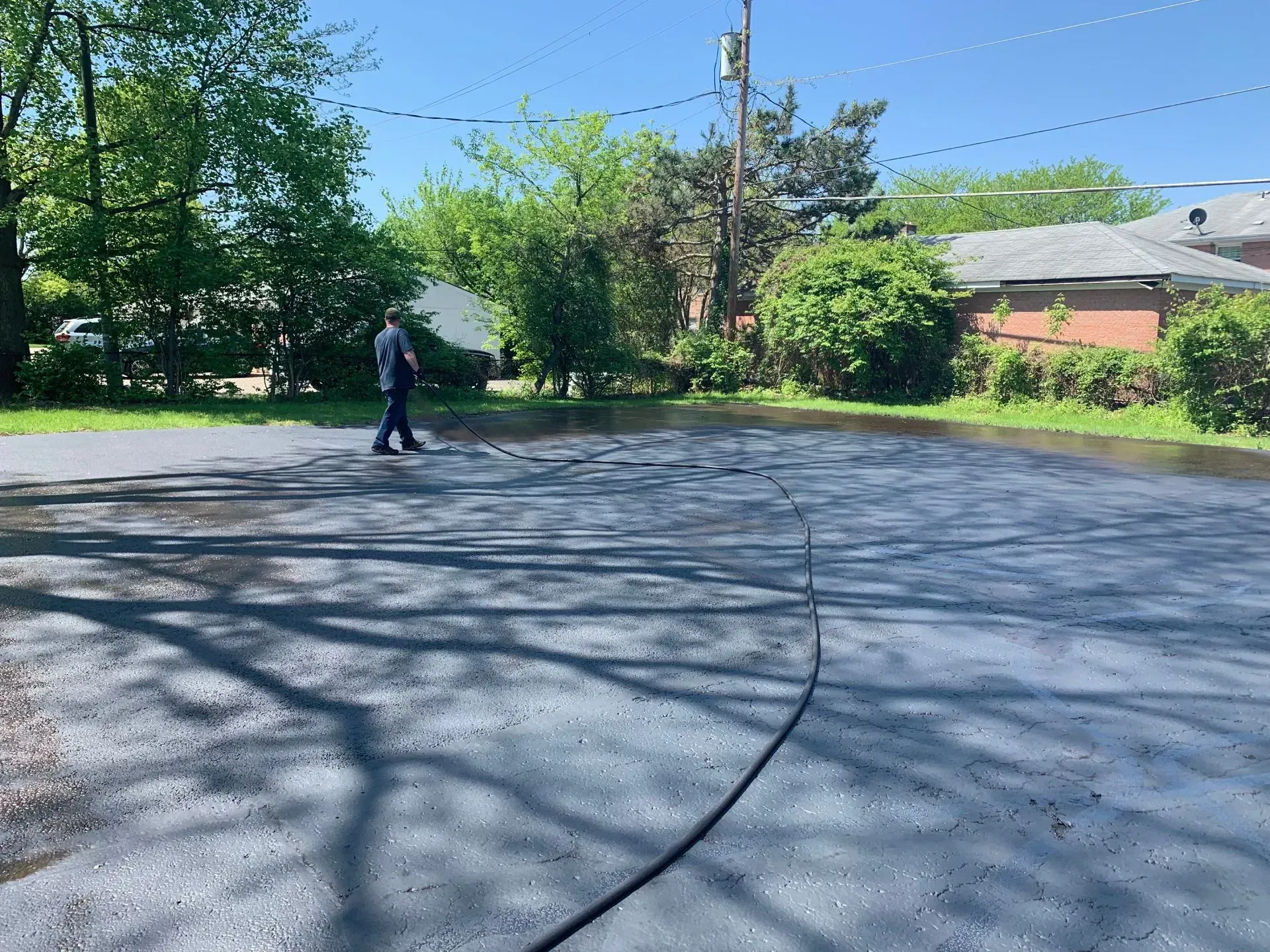 Person walking on a sunny paved road near trees and houses