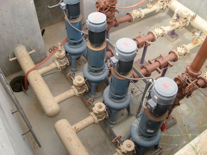 Industrial pump and pipe assembly with several blue motor units and tan piping in a concrete pit