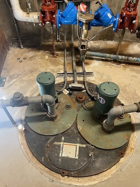 Industrial floor-mounted equipment with two green circular covers and connected pipes in a utility room
