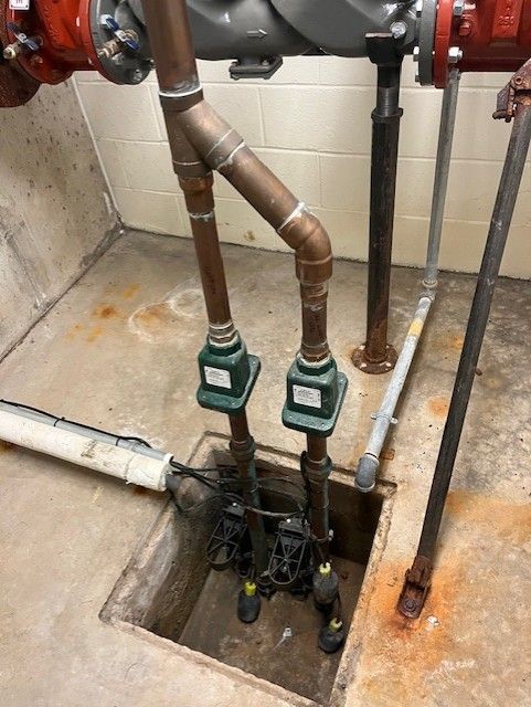 Basement plumbing with two green water meters and copper pipes against a concrete wall