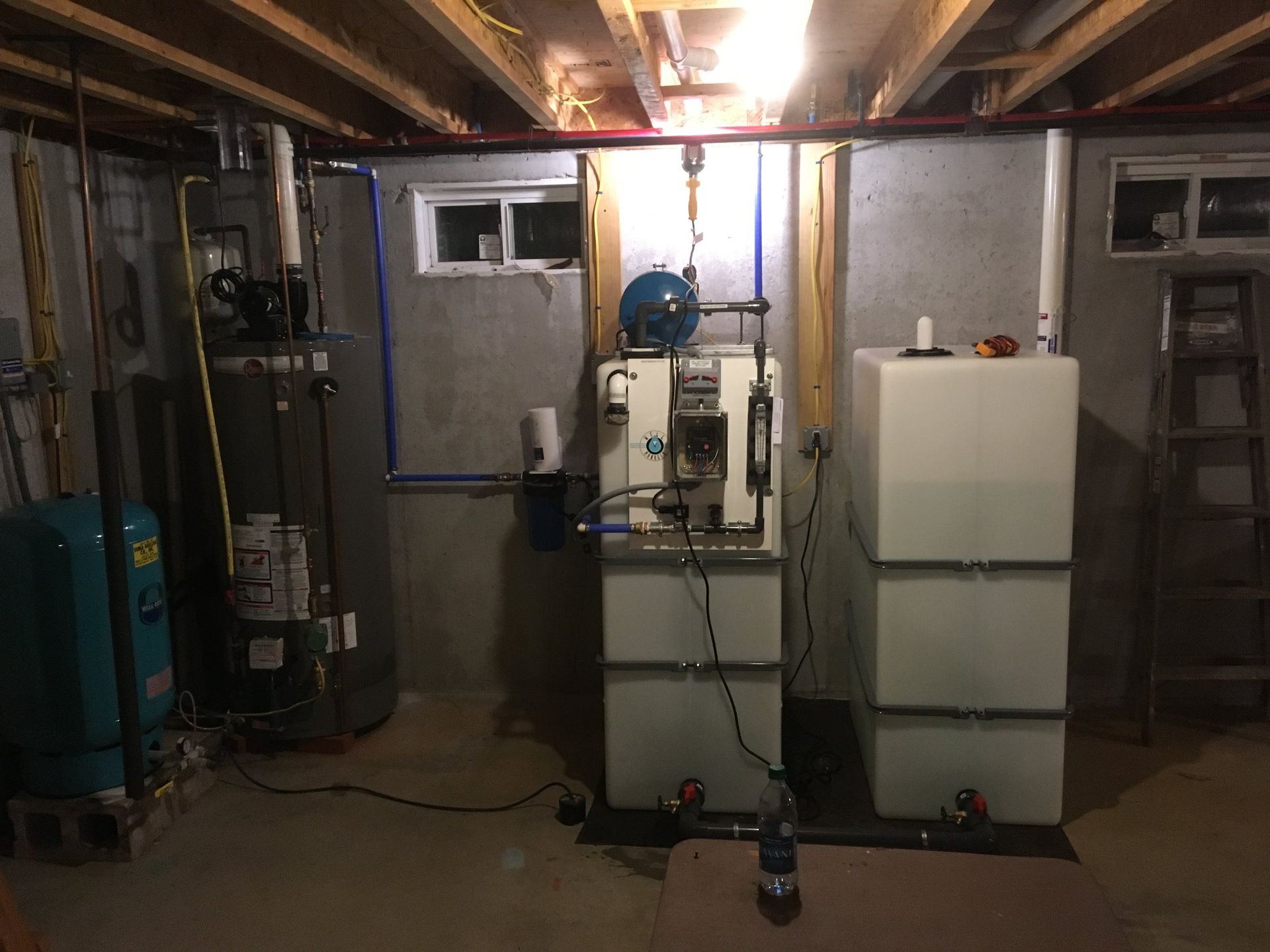 Basement mechanical room showing a water heater, a well pressure tank, water filtration equipment, and storage tanks.