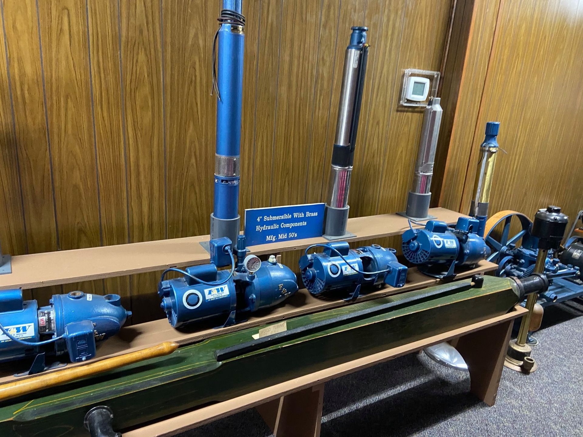 A display of various blue and metallic industrial water pumps and motors arranged on a wooden shelf.
