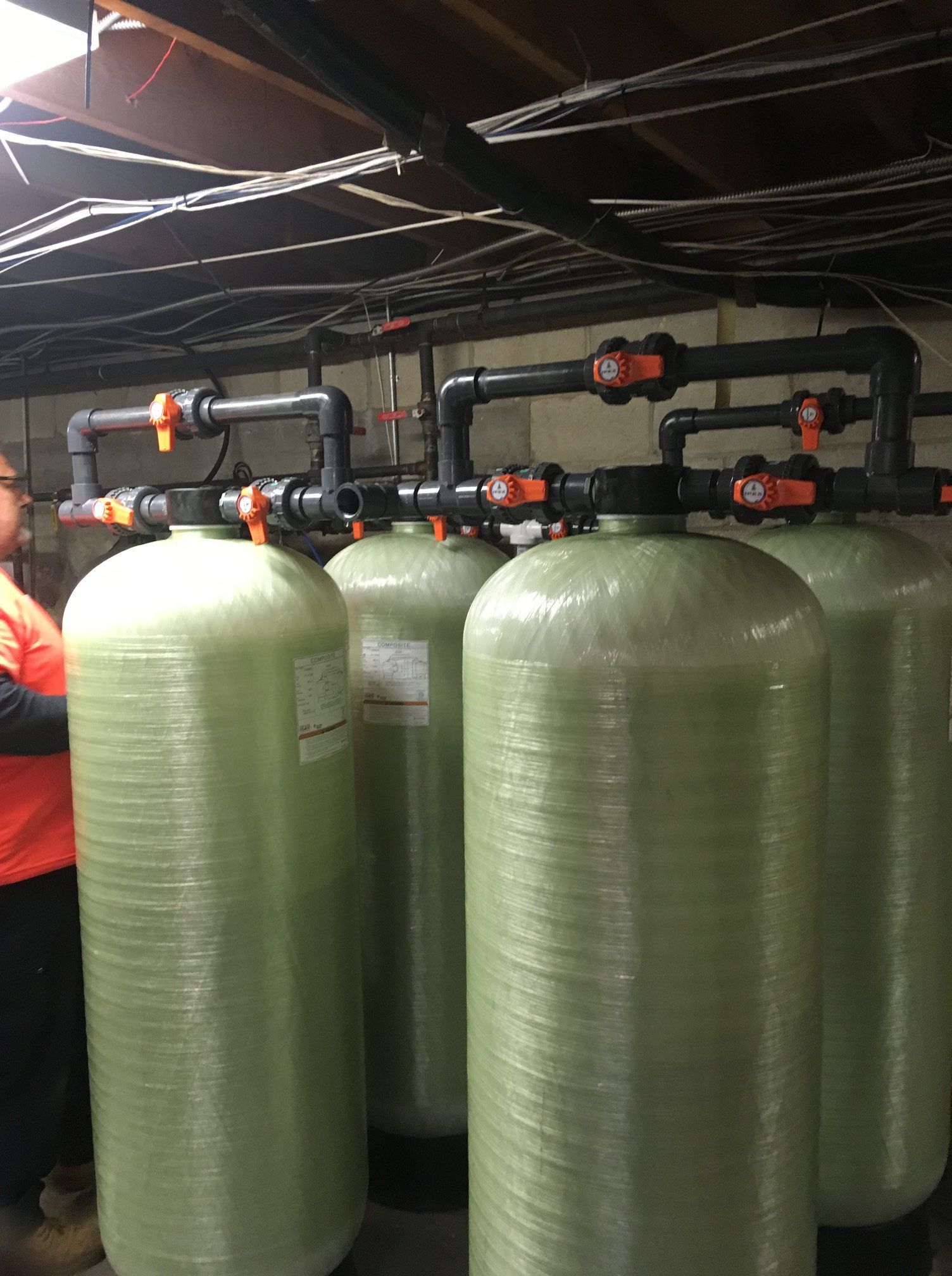 Four large, light-green industrial water filtration tanks arranged in a row with black piping and orange-handled valves.