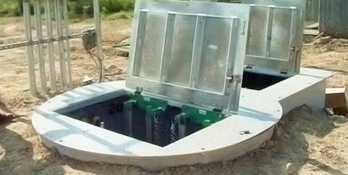 Open utility pit with metal lids in a dirt outdoor area