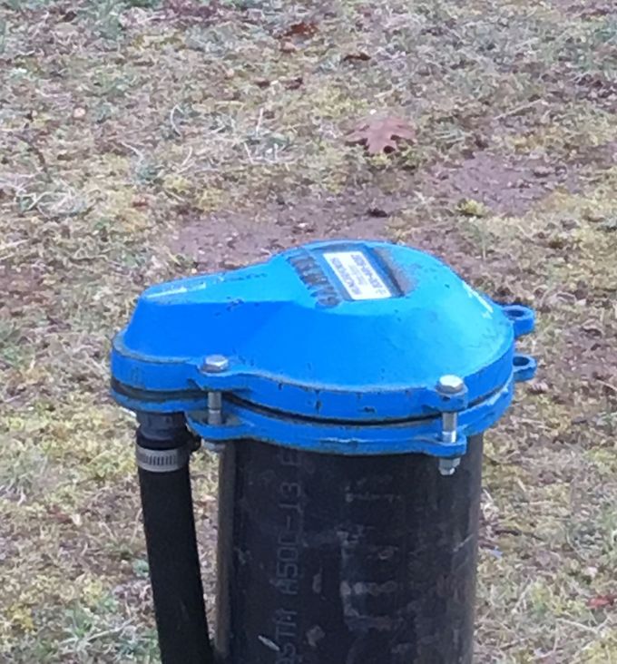 Blue-topped utility valve box on a black pipe in a grassy outdoor area