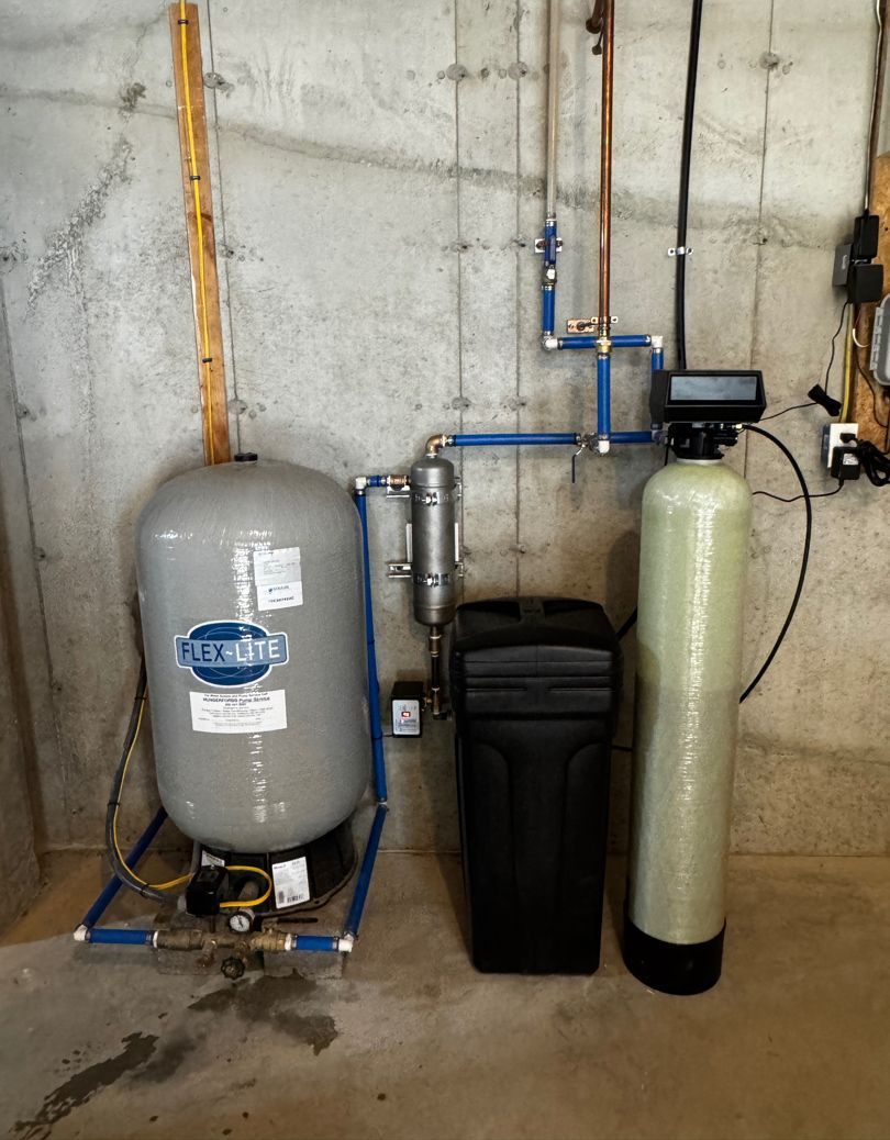Water softener and filtration system with tanks and plumbing against a concrete basement wall