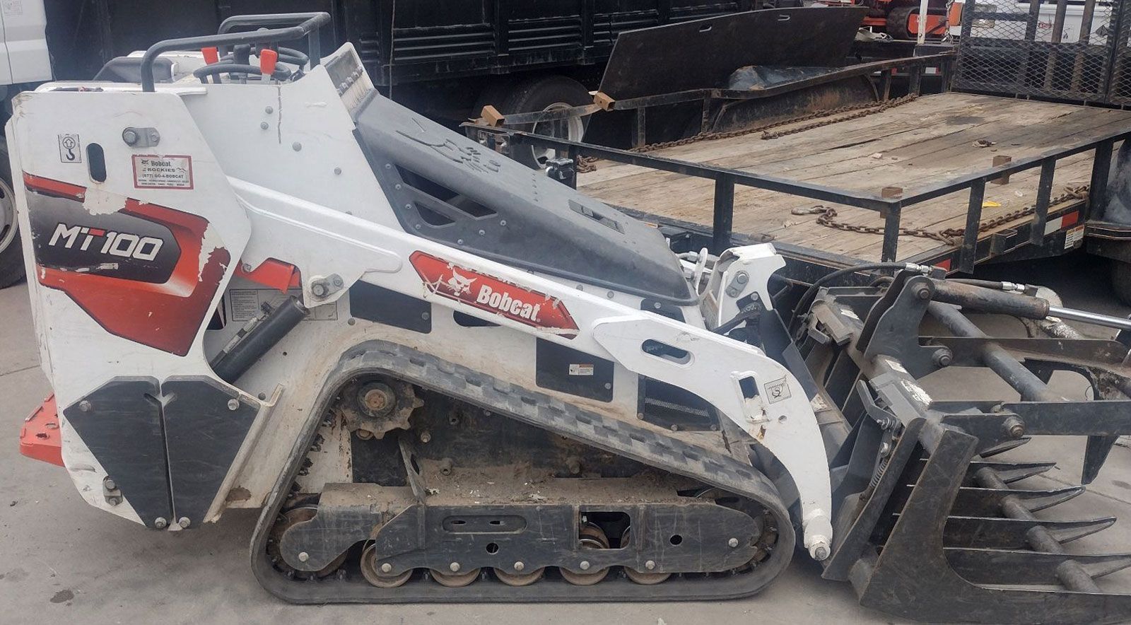 A bobcat tractor is parked next to a trailer.