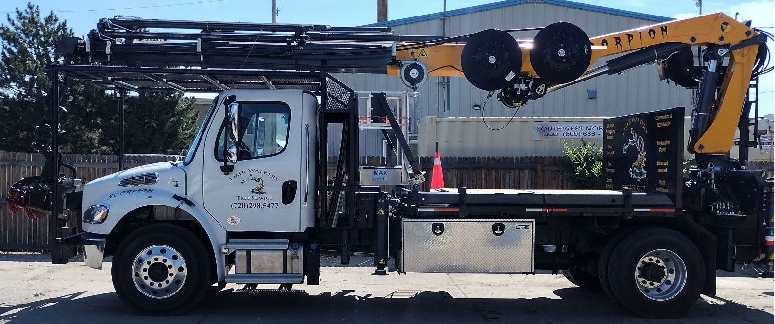 A white truck with a yellow crane on the back is parked in front of a building.