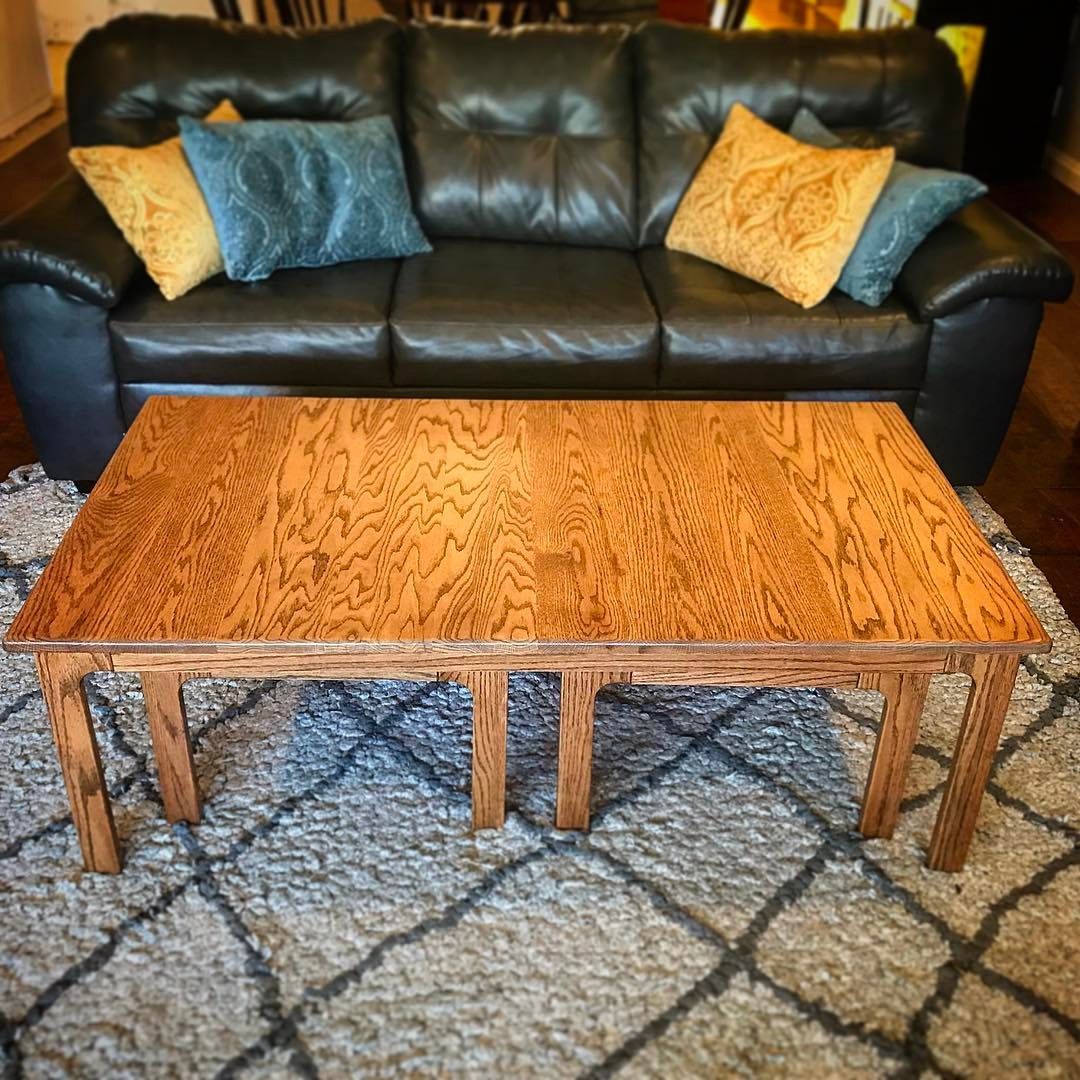 Wooden coffee table in front of a leather sofa with colorful pillows on a patterned rug.