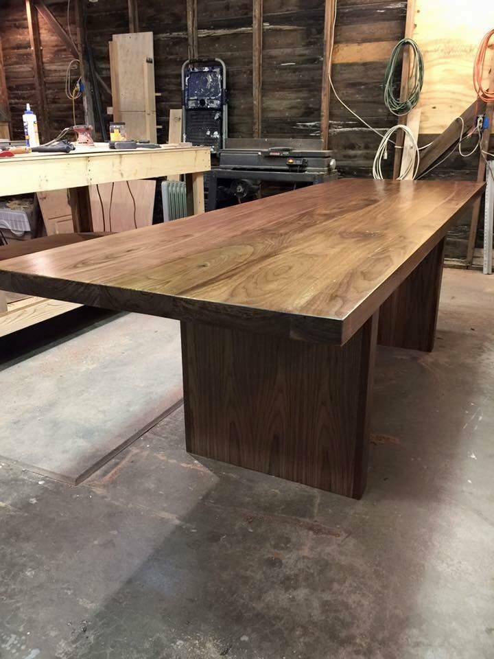 Wooden dining table in a workshop, with two dark-stained legs supporting a long, dark wood surface.