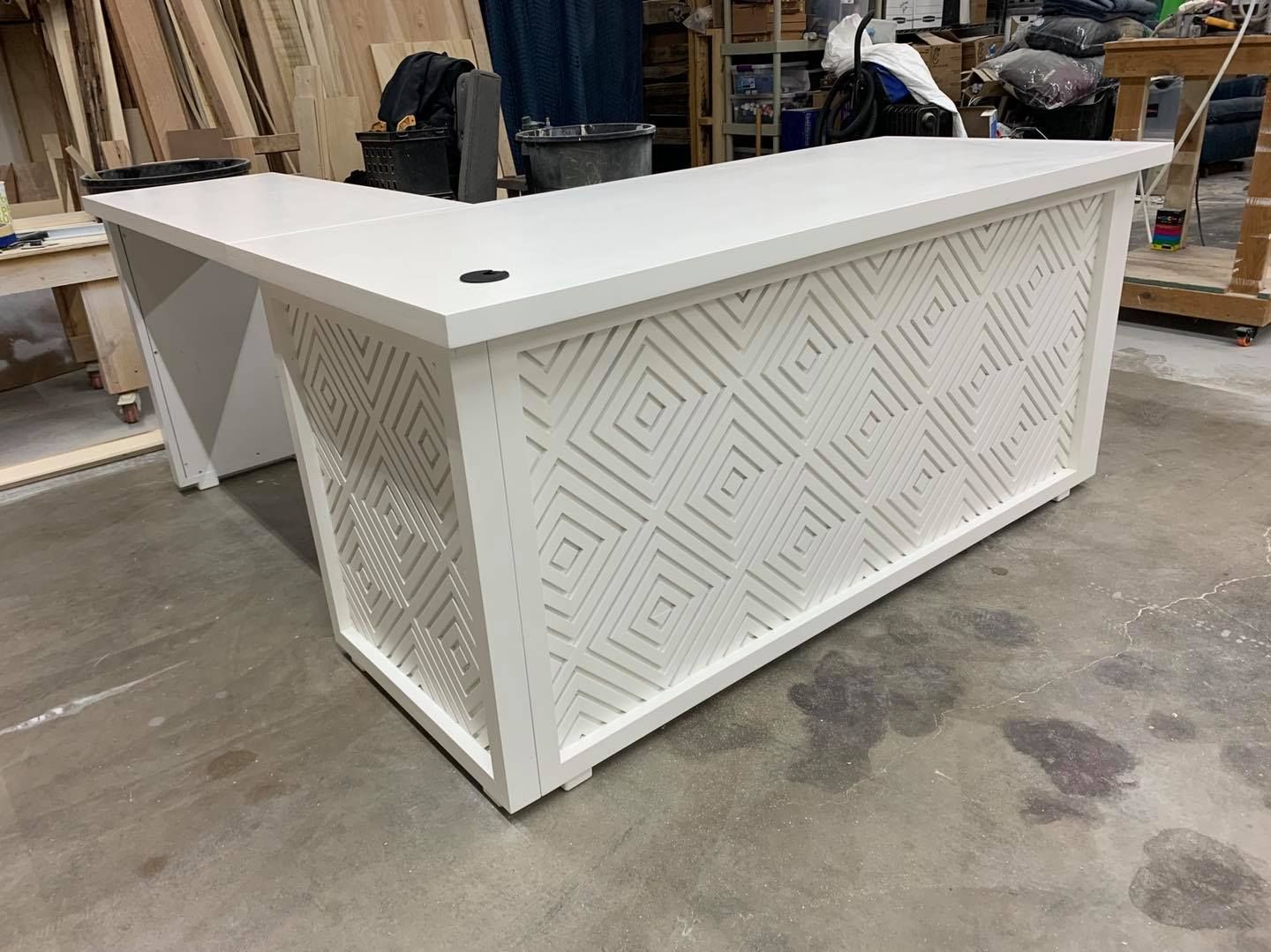White L-shaped desk with geometric lattice paneling, in a workshop setting.