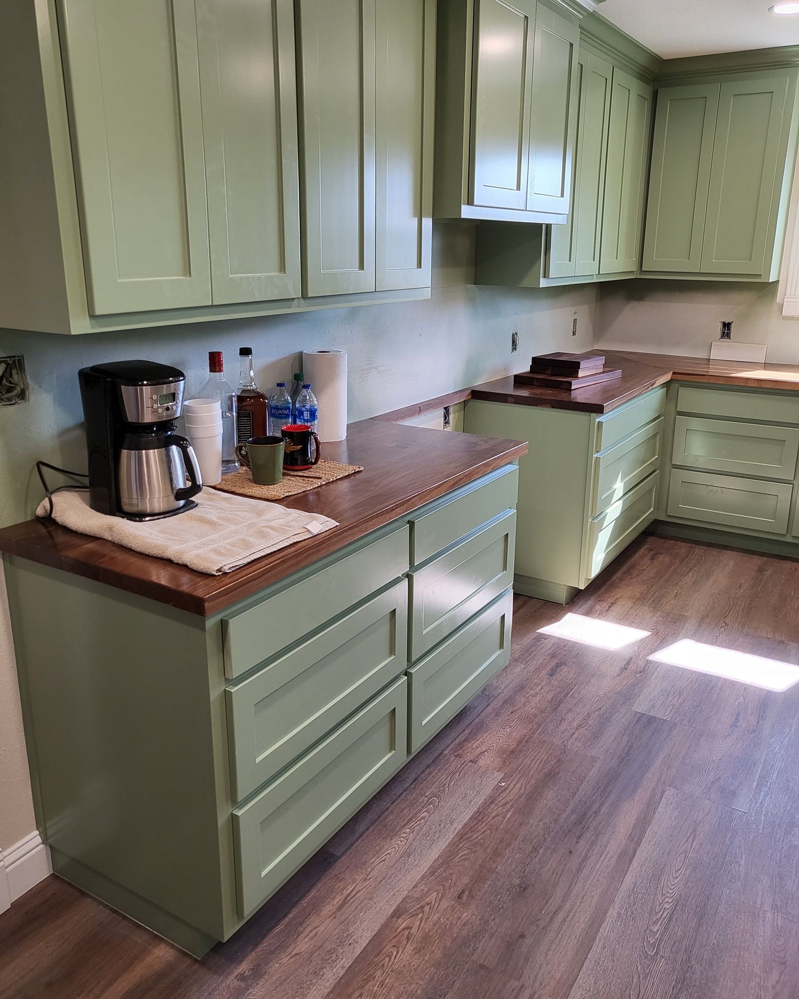 Green kitchen cabinets with wooden countertops and a coffee maker.