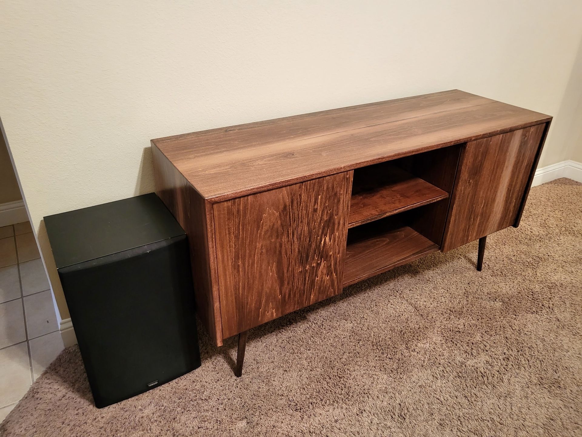 Wooden TV console and black subwoofer on a carpeted floor.