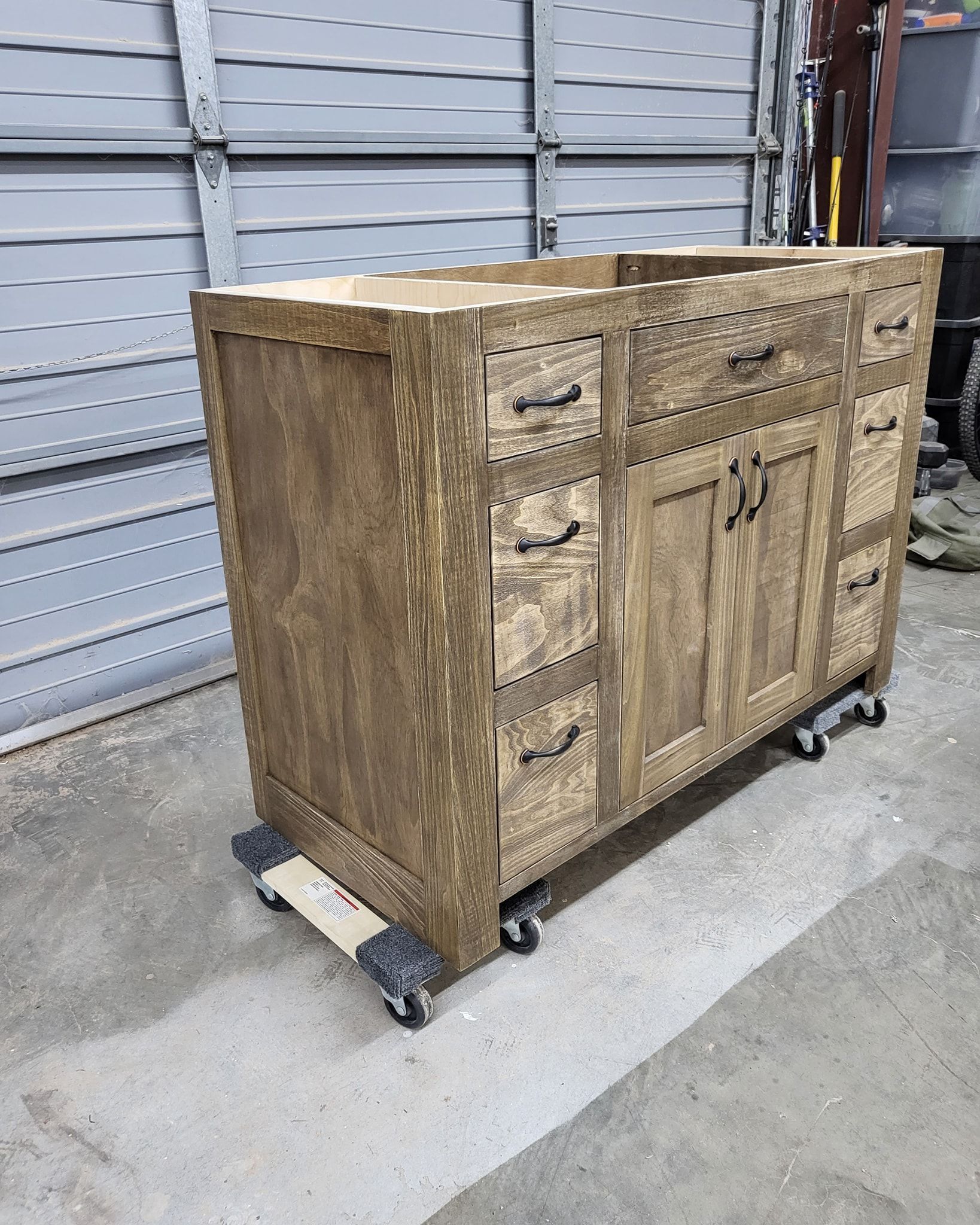 Wooden bathroom vanity with drawers and doors, stained brown, on a rolling platform.