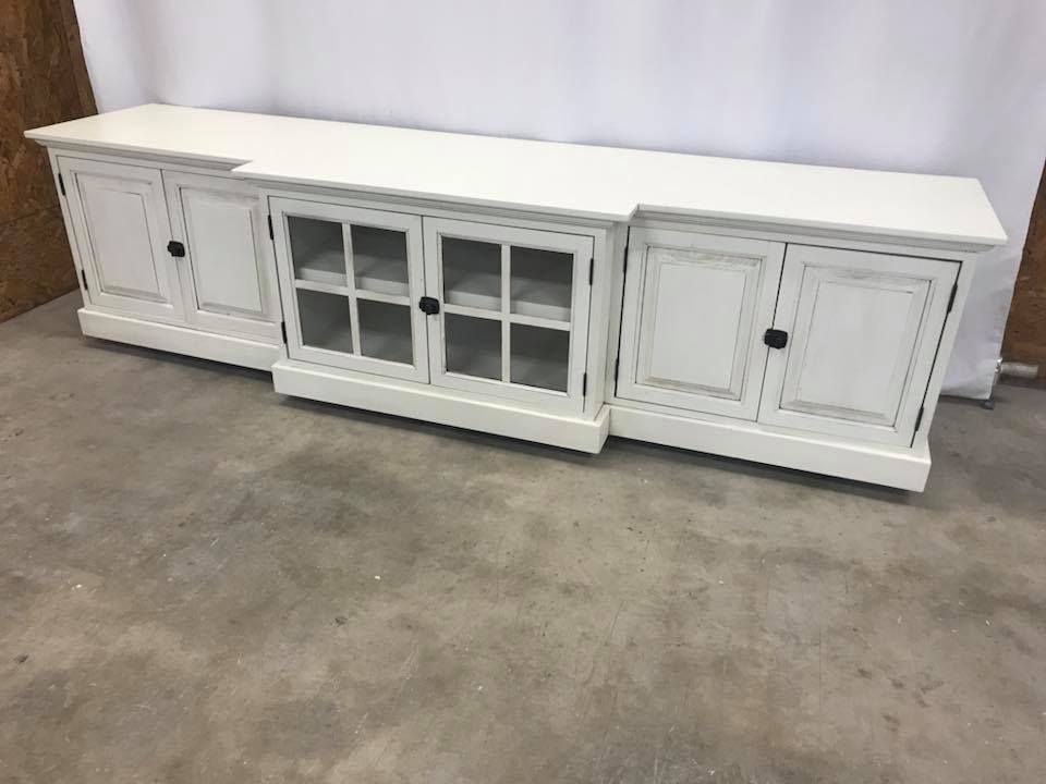 White wooden media console with cabinet doors and glass-paned center section, set on a gray surface.