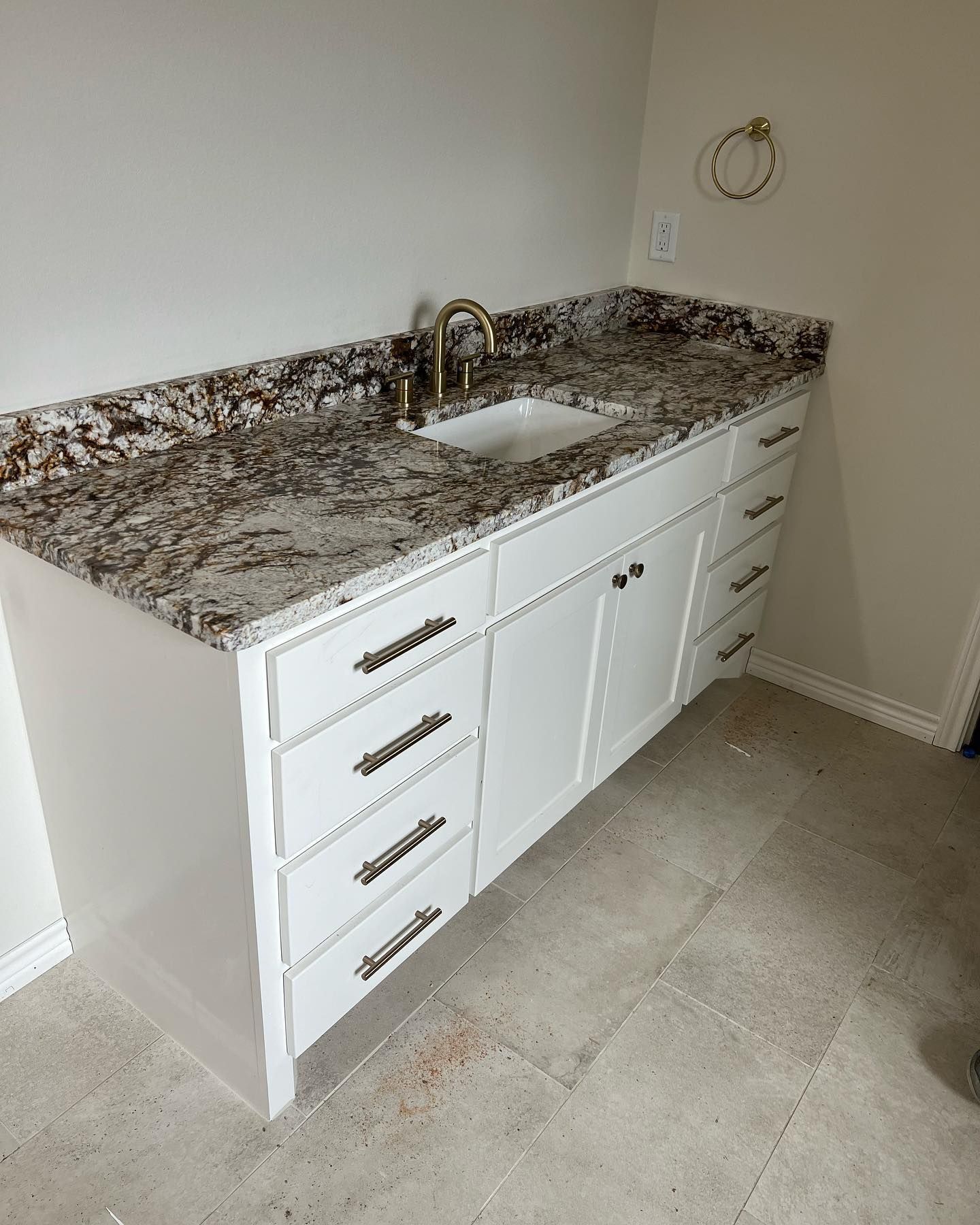 White bathroom vanity with granite countertop and gold faucet.
