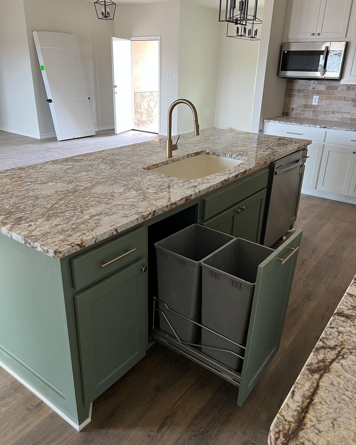 Green kitchen island with granite countertop, sink, and pull-out trash bins.
