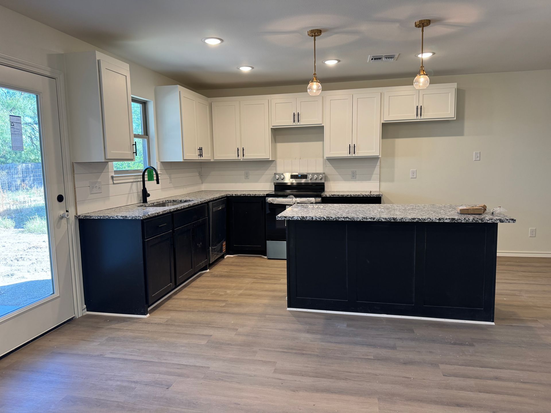 Modern kitchen with white and navy cabinets, granite countertops, and wood-look flooring.