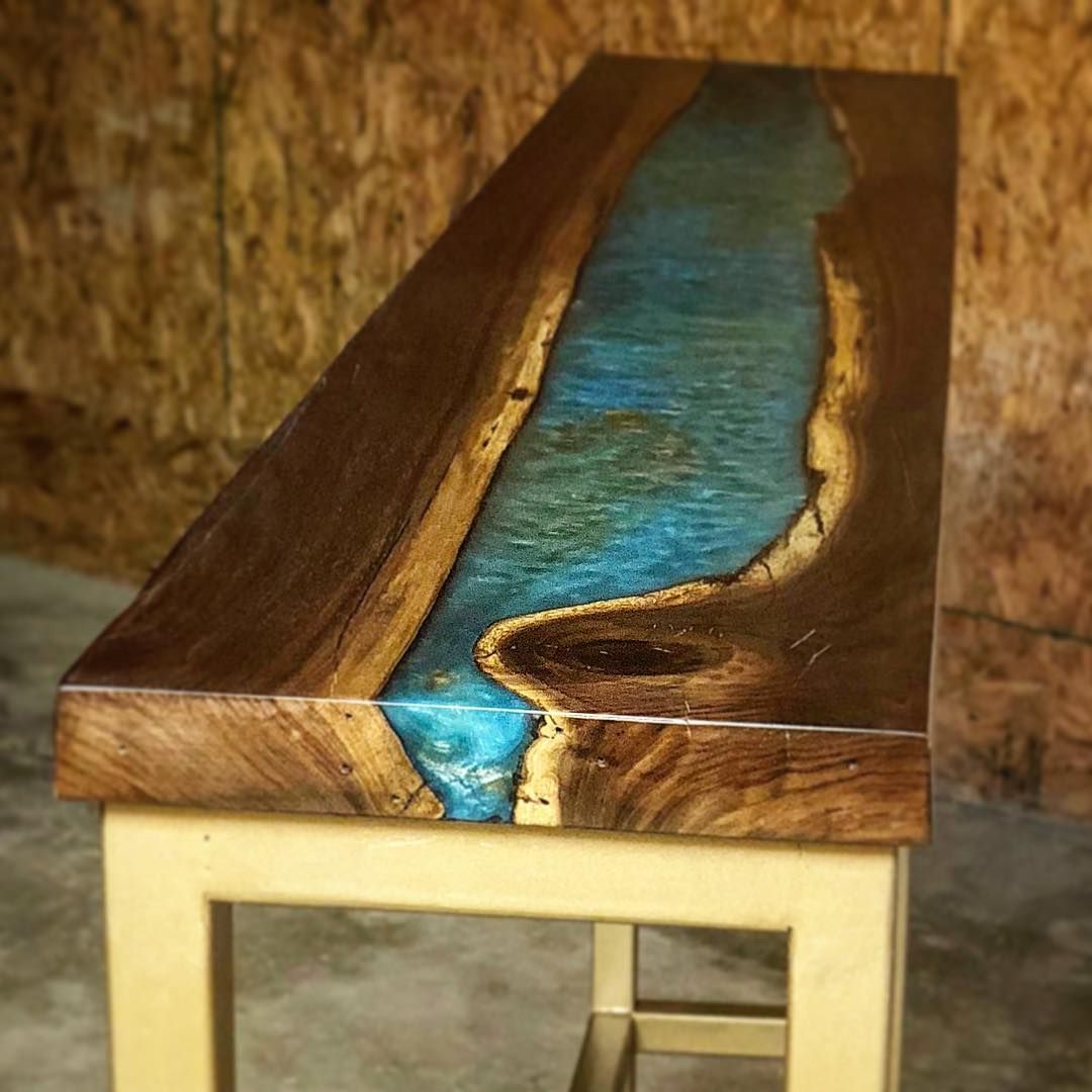 Wooden table with turquoise resin river in the center, resting on a beige metal base.