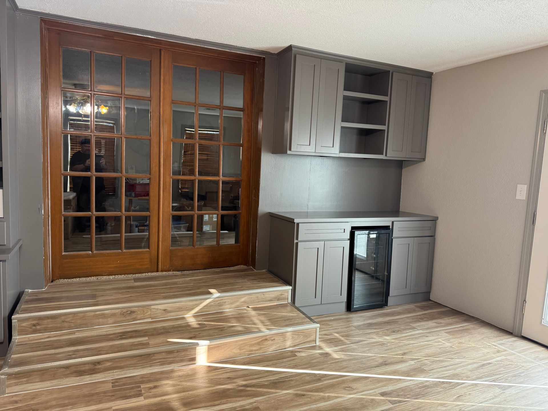 Interior space with hardwood floors, cabinets, and double doors. A small refrigerator is built into the cabinets.