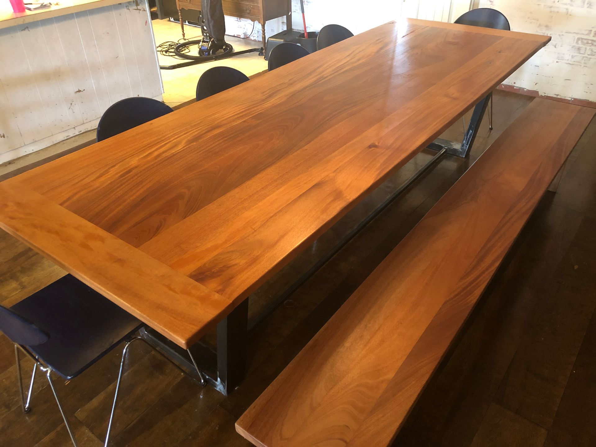 Long, wooden table with bench and chairs; a modern design with a shiny finish and metal legs.