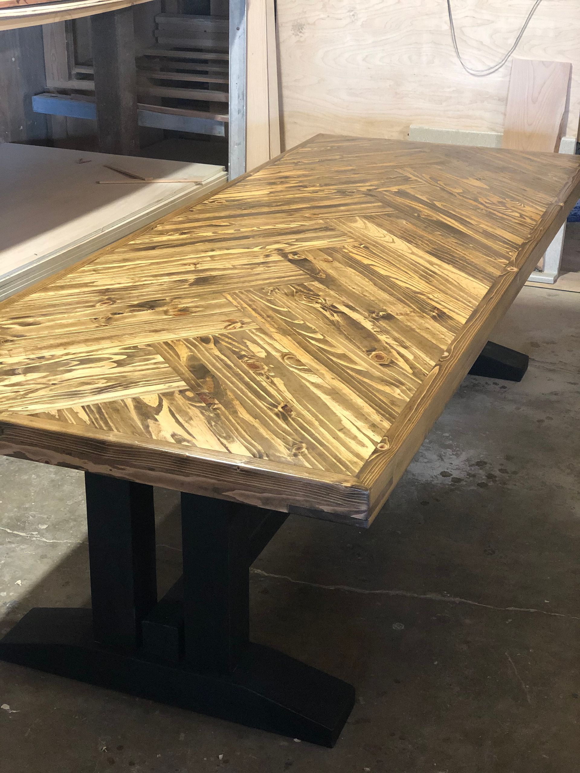 Wooden table with a herringbone pattern top and black trestle base.