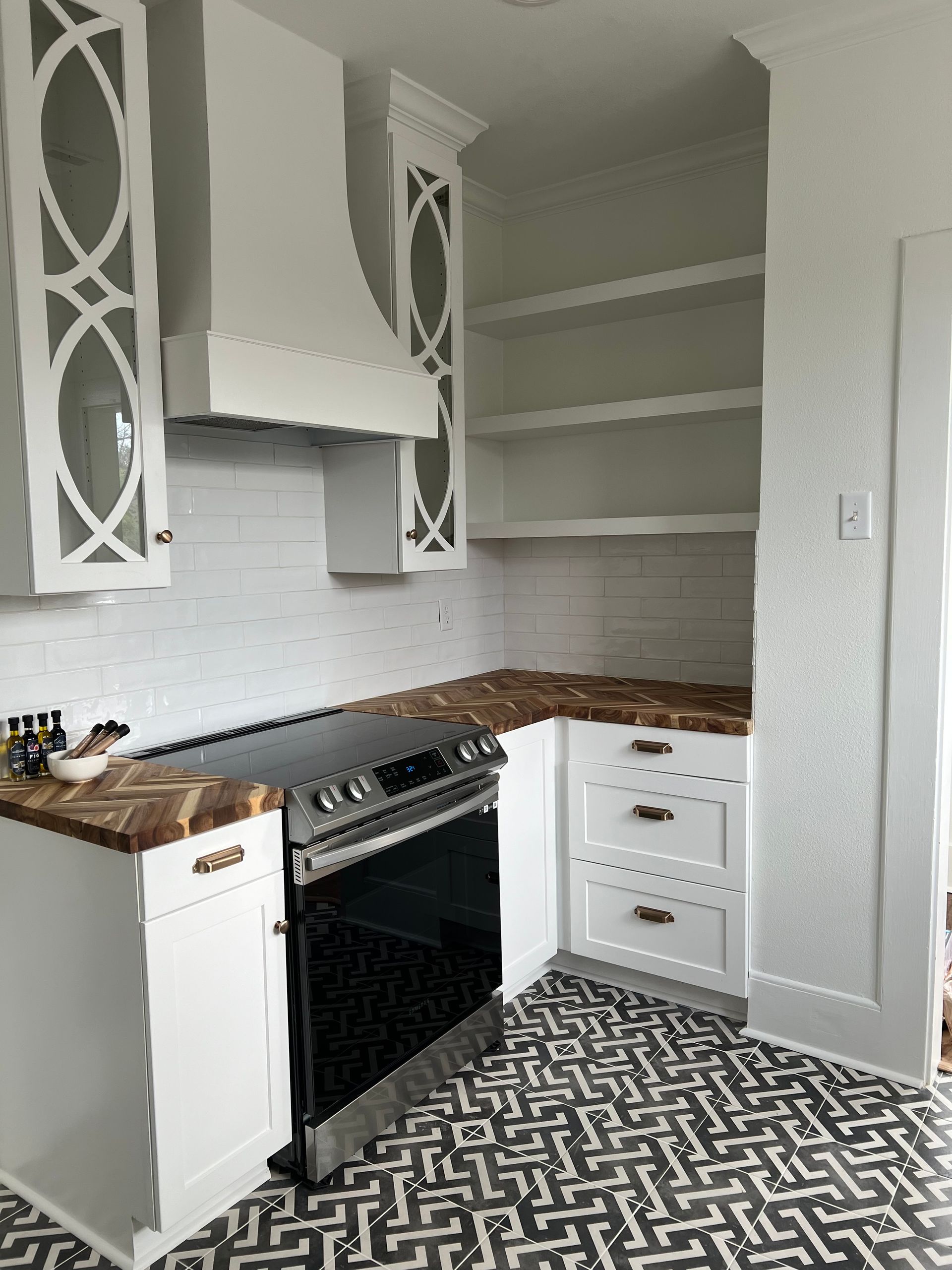 White kitchen with patterned floor, white cabinets, range, and open shelving.